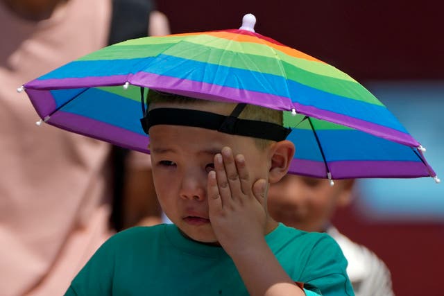 <p>A boy wearing a rainbow umbrella wipes his sweat as he visits the Forbidden City on a sweltering day in Beijing on Friday</p>