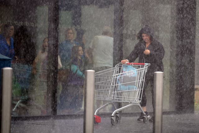 A woman is caught in heavy rain in Speke, Liverpool (PA)