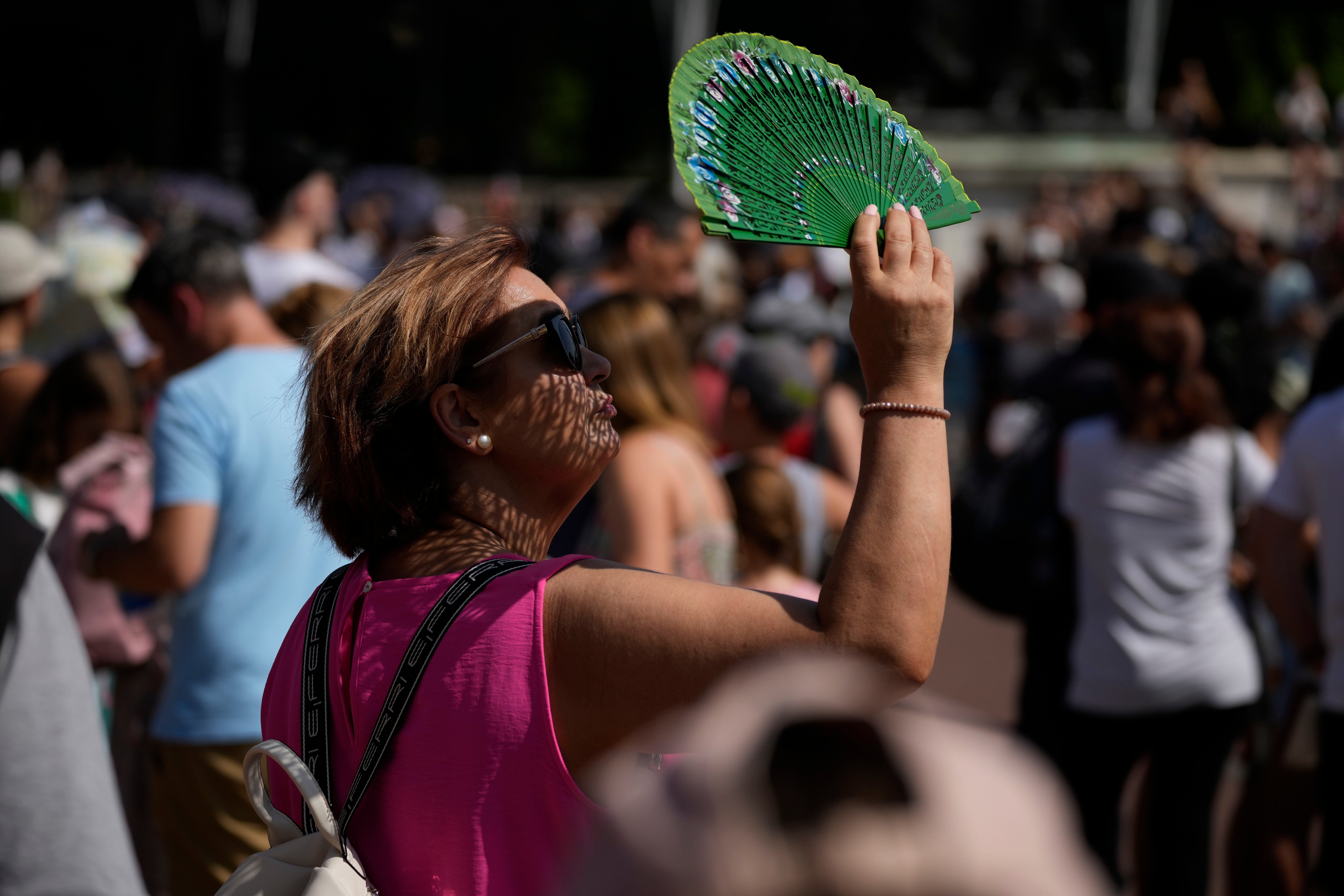 A tourist uses a fan to shade her face from the sun