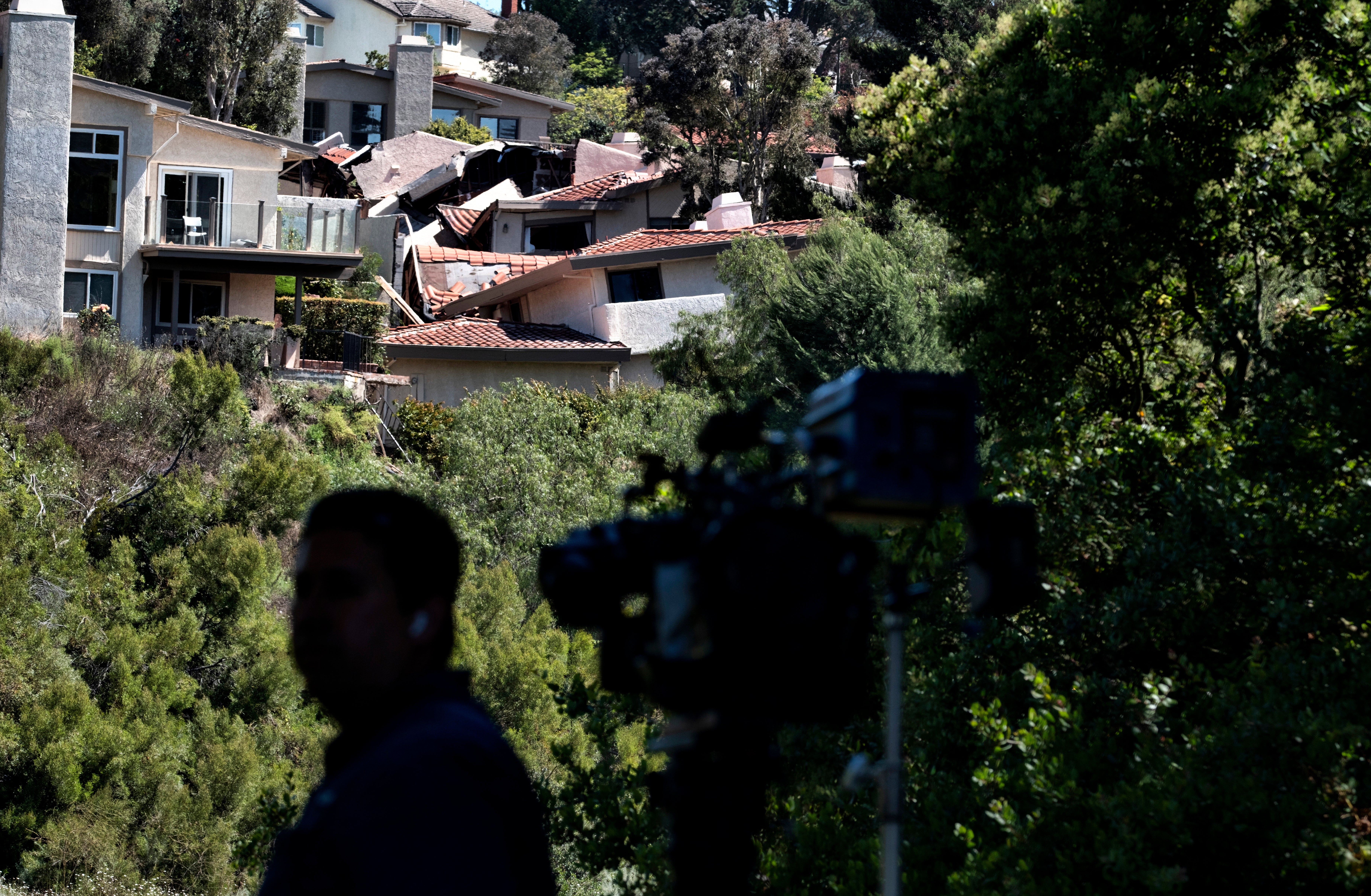 A television news cameraman gets ready for a live broadcast across a ravine from severely damaged homes in Rolling Hills Estates on the Palos Verdes Peninsula in Los Angeles County