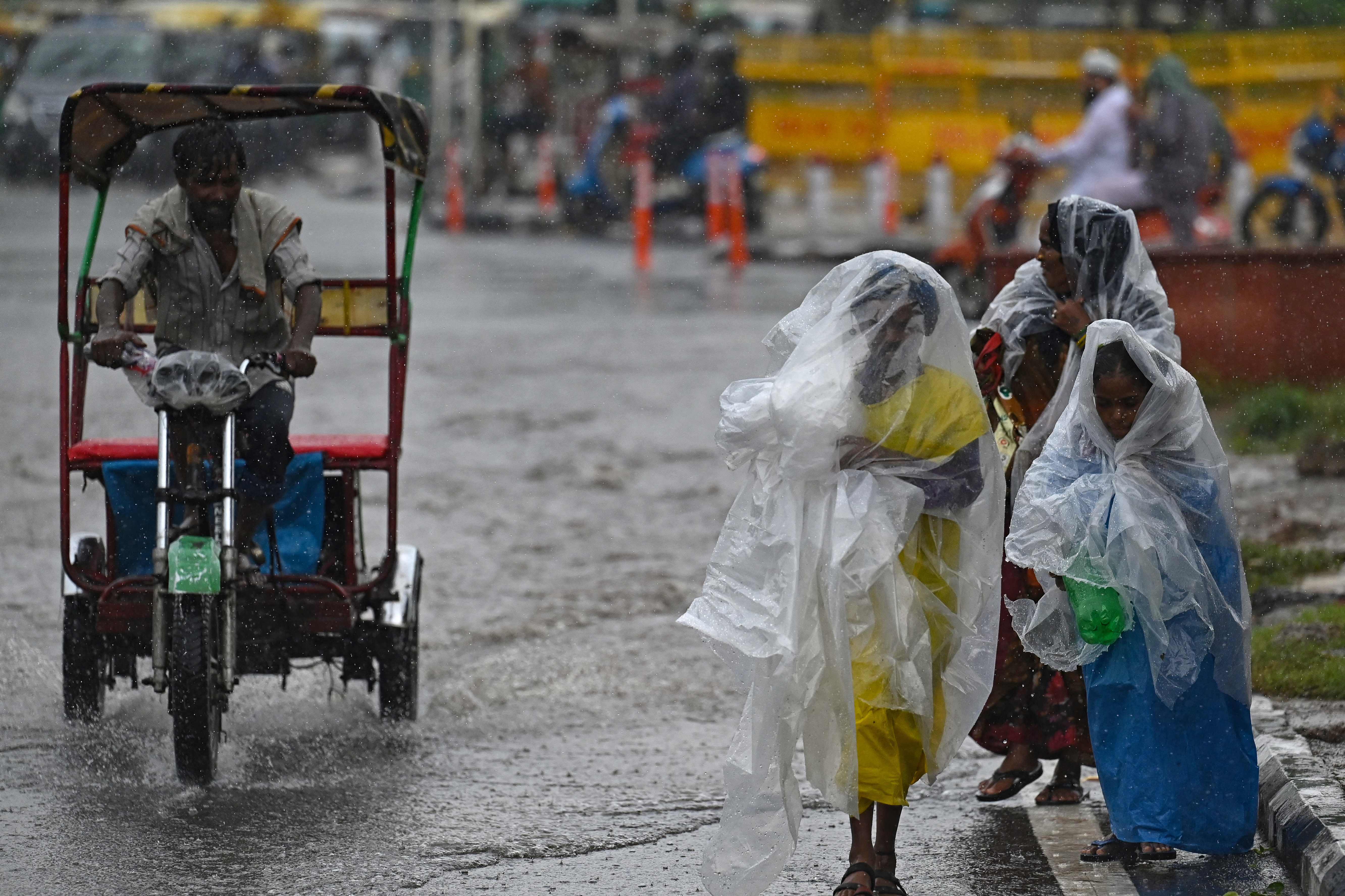 Commuters use plastic sheets to protect themselves from rain in New Delhi