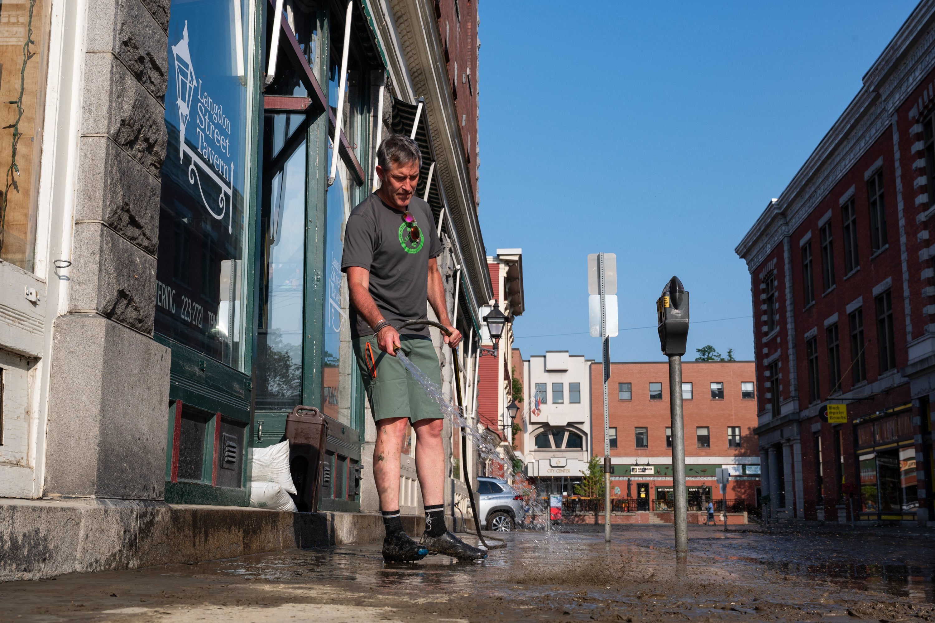 Andrew Brewer, a resident of Montpelier and former business owner on Langdon Street, helps wash away the mud from the sidewalk