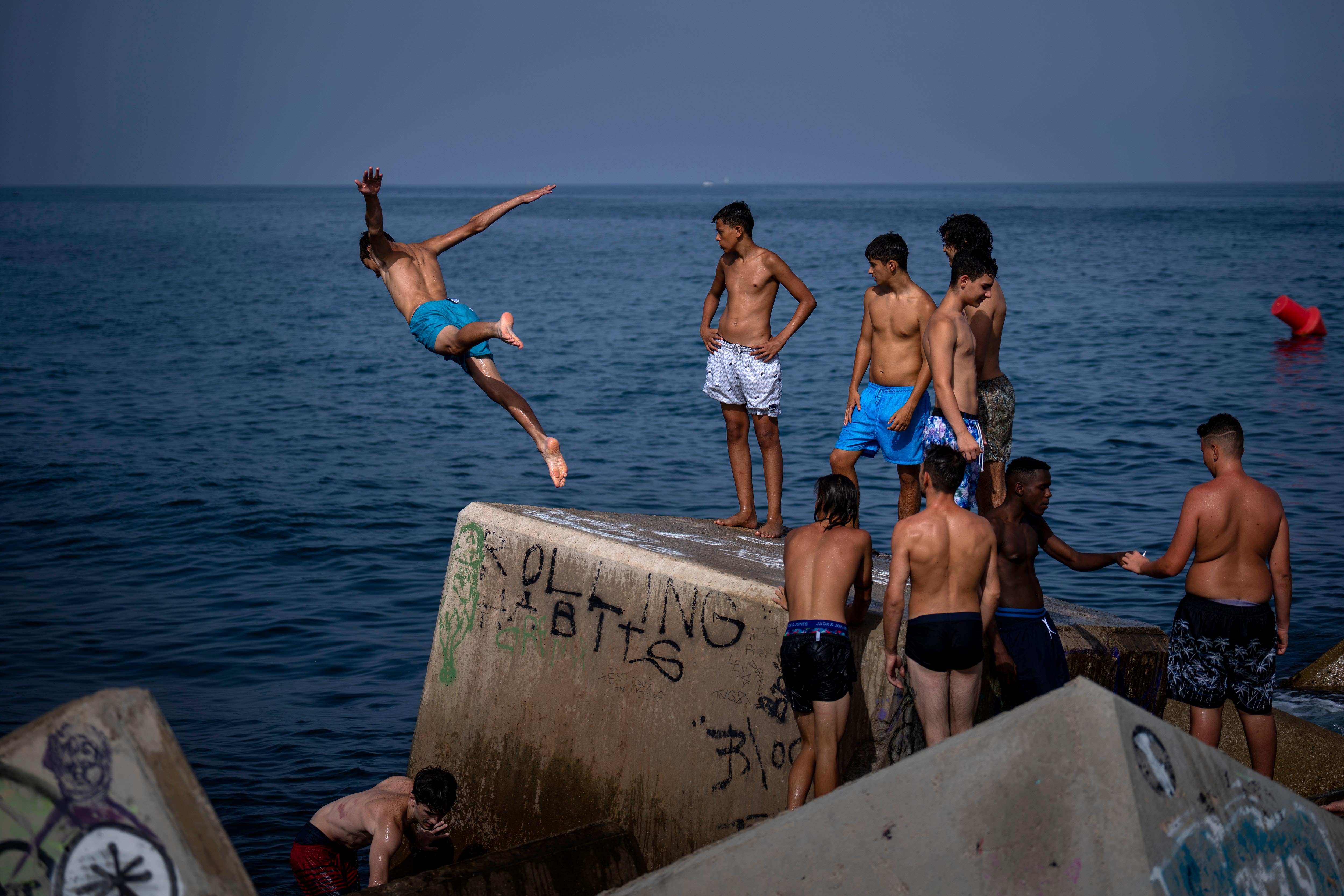 A youth jumps into the sea on a breakwater in Barcelona (AP Photo/Emilio Morenatti)