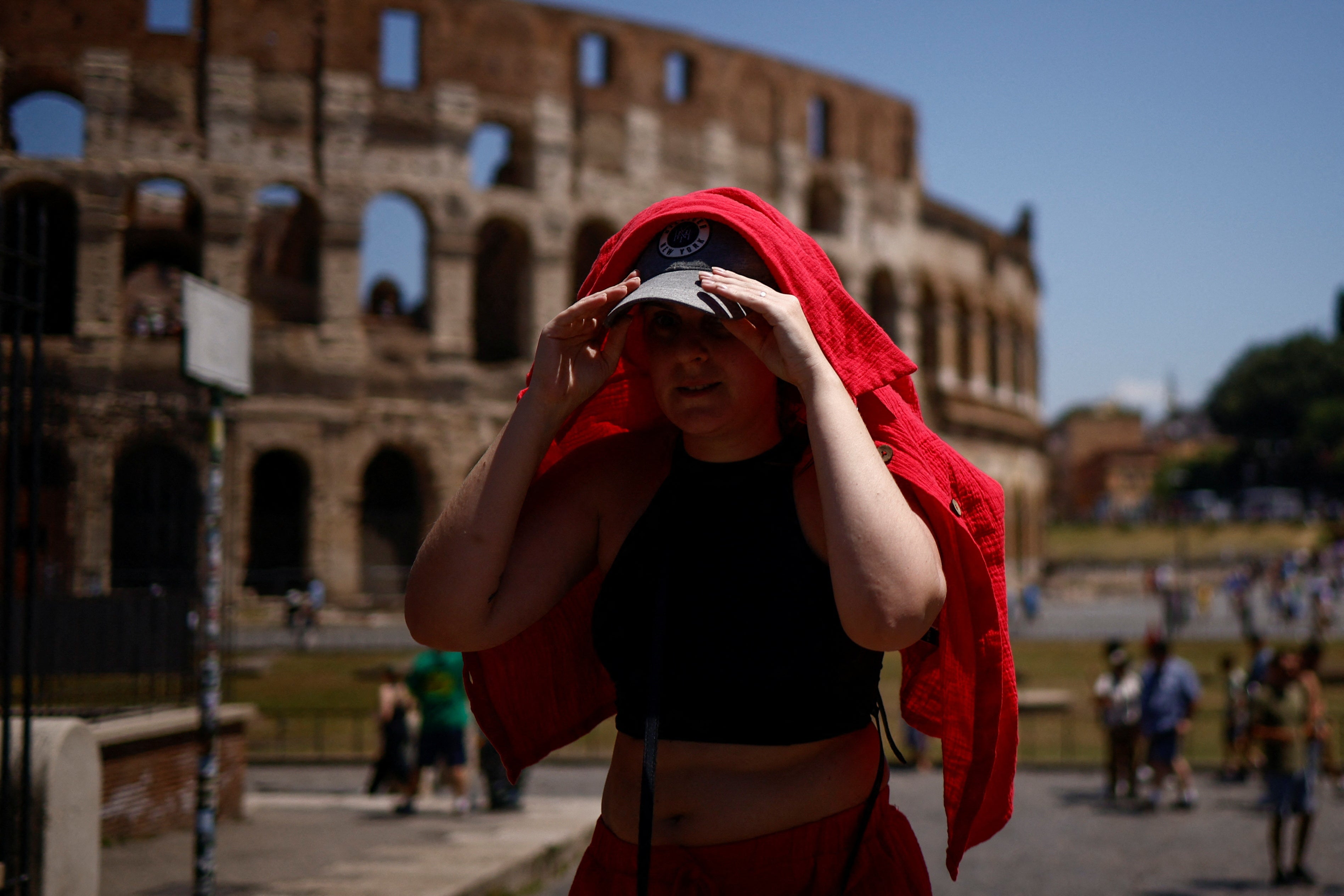 A woman shelters from the sun with a shirt near the Colosseum in Rome