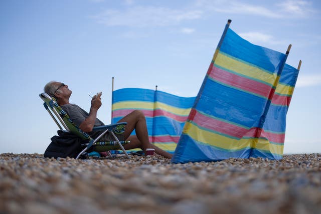 <p>A man sits behind a wind-break on the beach </p>