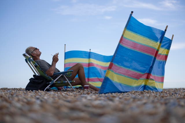 <p>A man sits behind a wind-break on the beach </p>