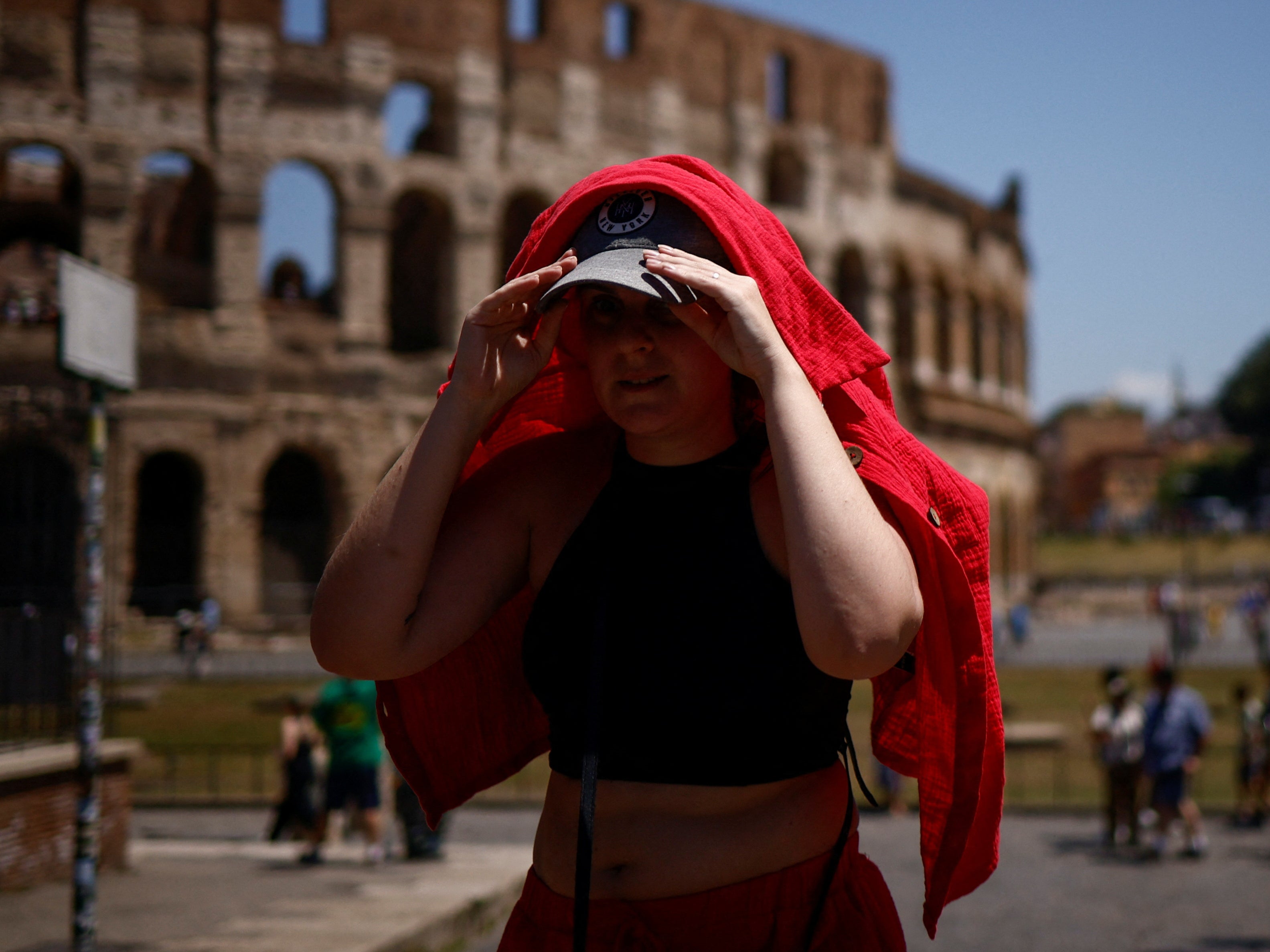 <p>A woman shelters from the sun with a shirt near the Colosseum during a heatwave across Italy</p>