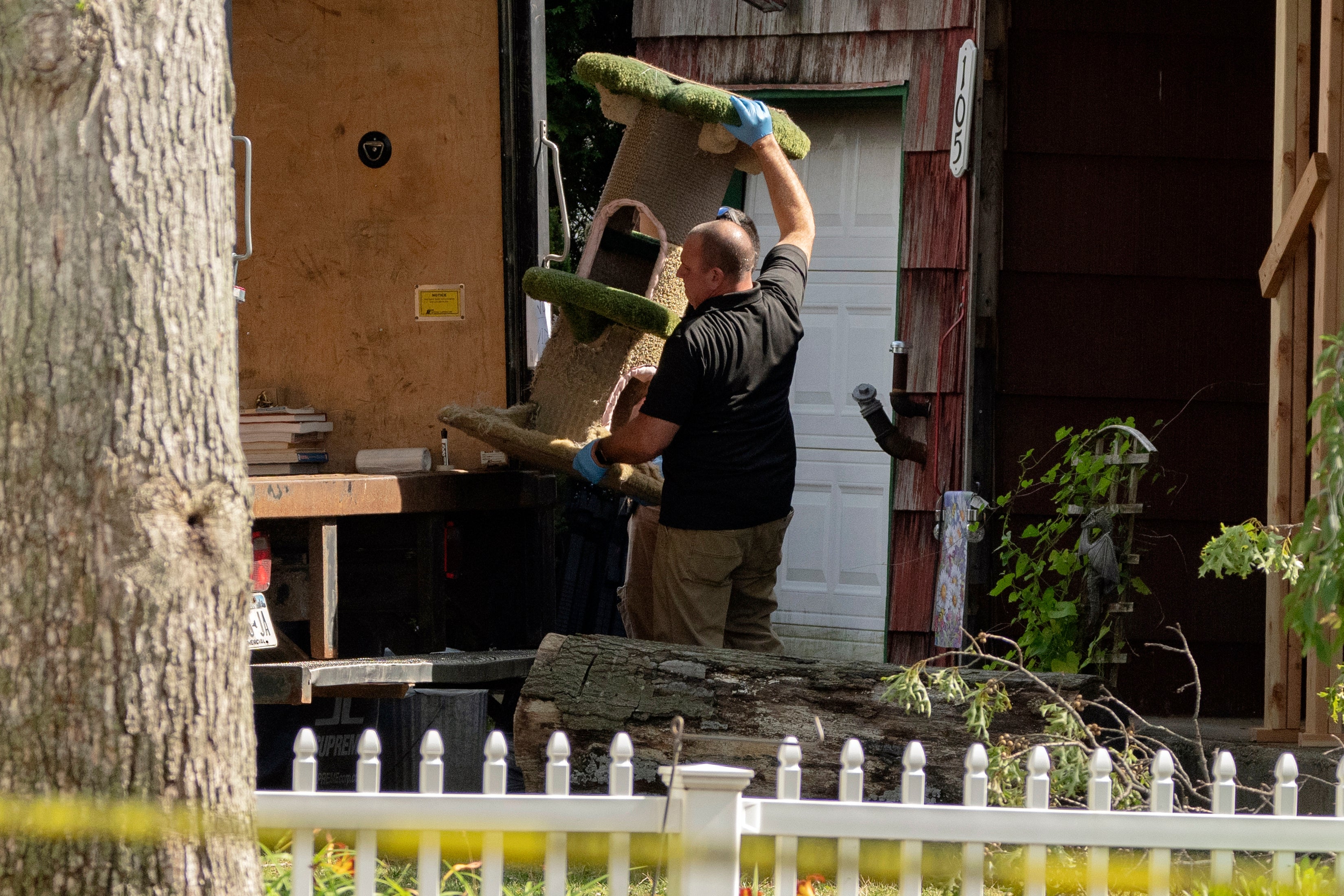 A crime laboratory officer moves a cat scratching post as law enforcement searches the home of Rex Heuermann