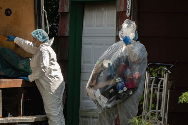 <p>A crime laboratory officer moves a plastic bag of items as law enforcement searches the home of Rex Heuermann on Saturday</p>