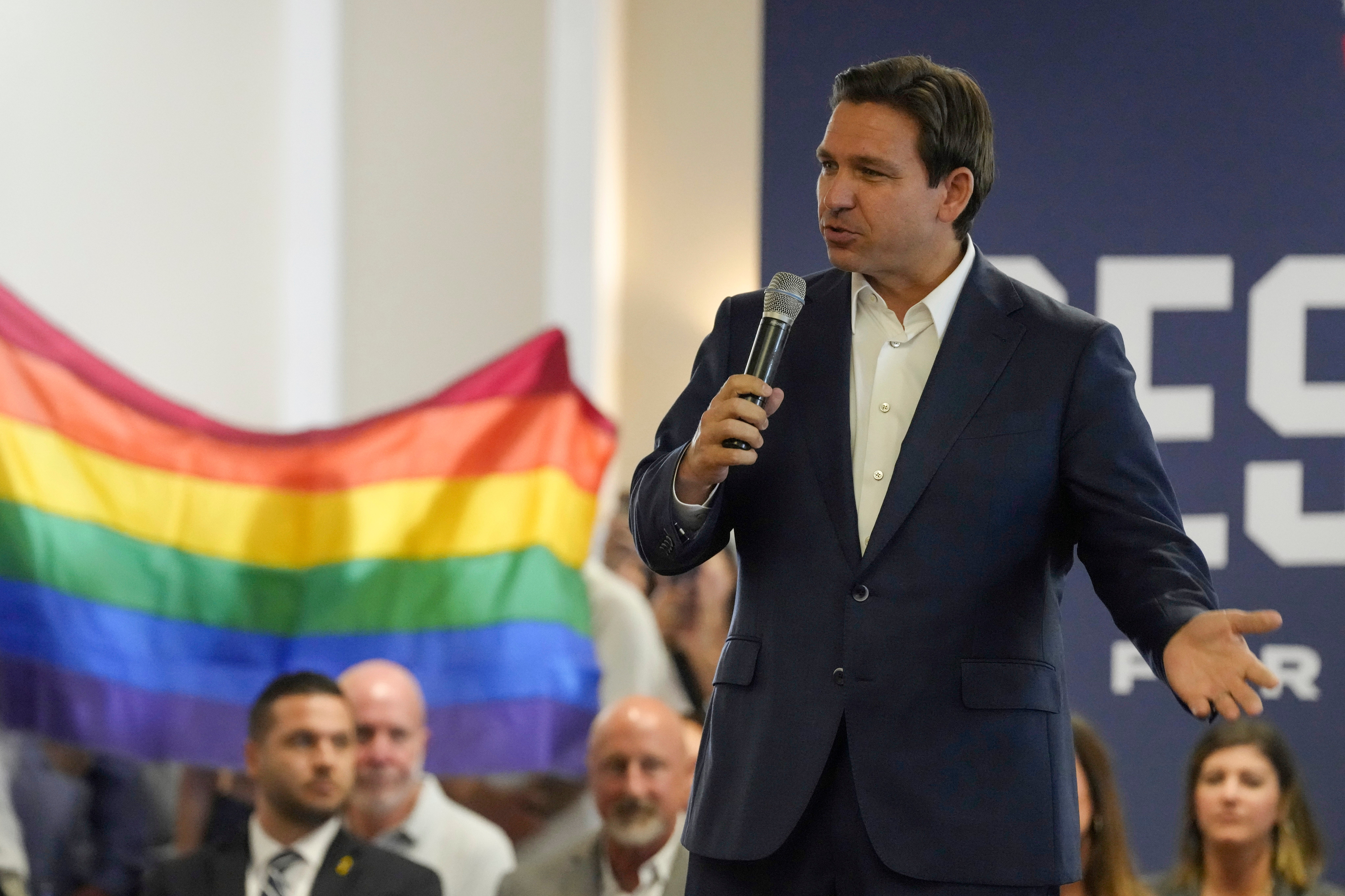 Protesters unfold and raise a rainbow flag behind Florida governor Ron DeSantis during the GOP presidential candidate’s campaign event