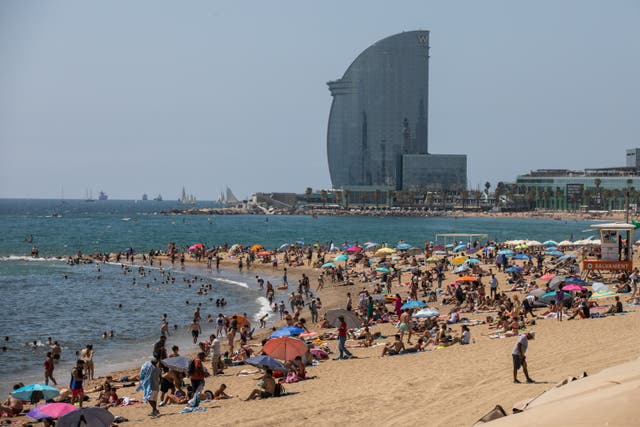 <p>Sunbathers enjoy the sun on Barceloneta beach with the W Barcelona hotel in the background </p>