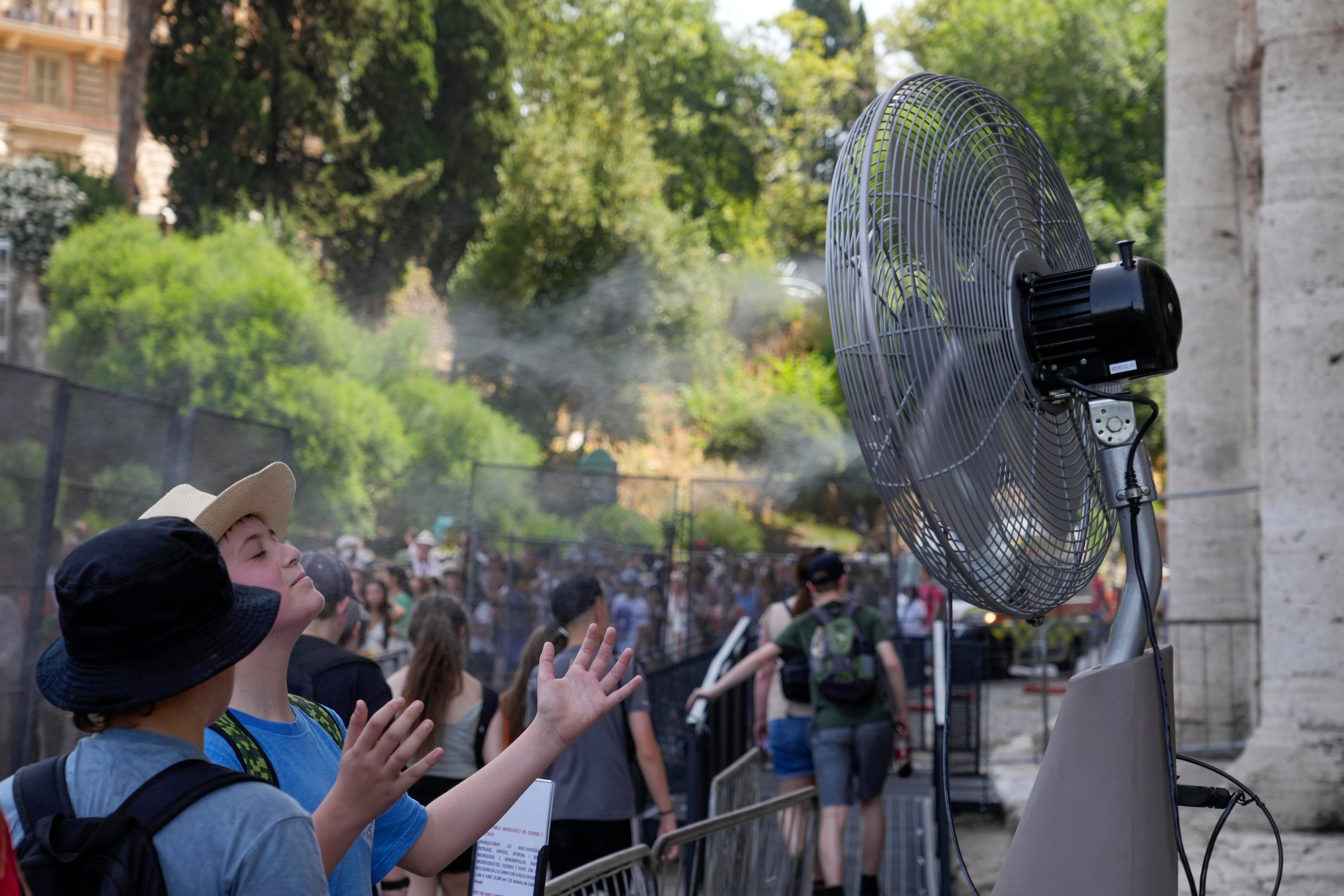 Tourists cool off near fan as they queue to enter Rome's Colosseum