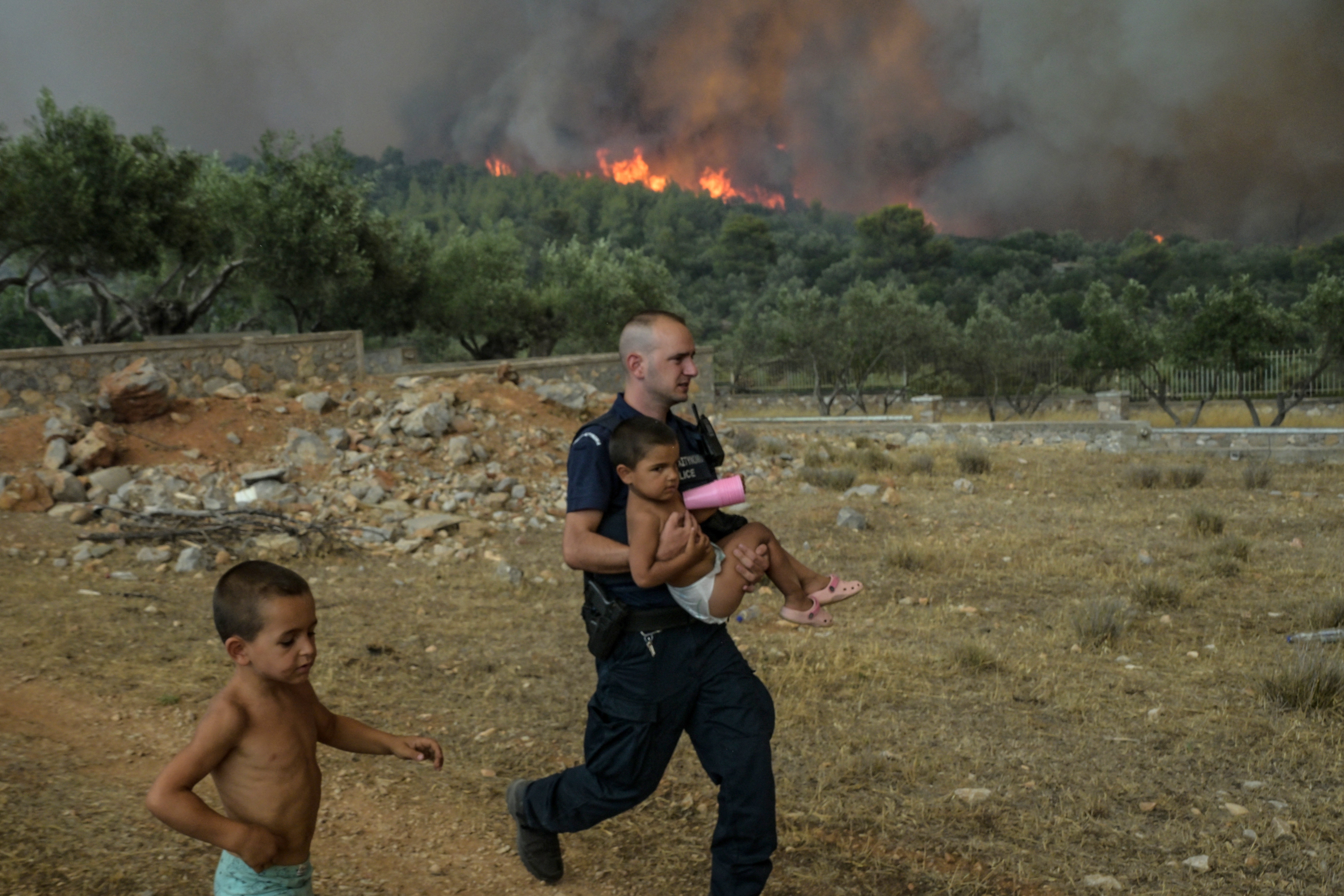 A Greek policeman evacuates a child from wildfire at the village of Agios Charamlabos, near the capital Athens