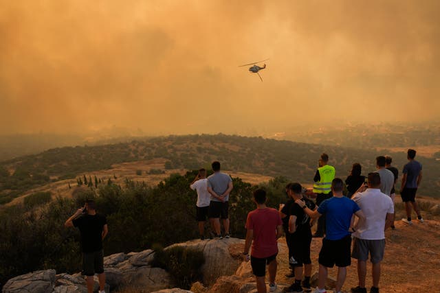 <p>A firefighting helicopter flies through smoke as people look on in Mandra, west of Athens</p>