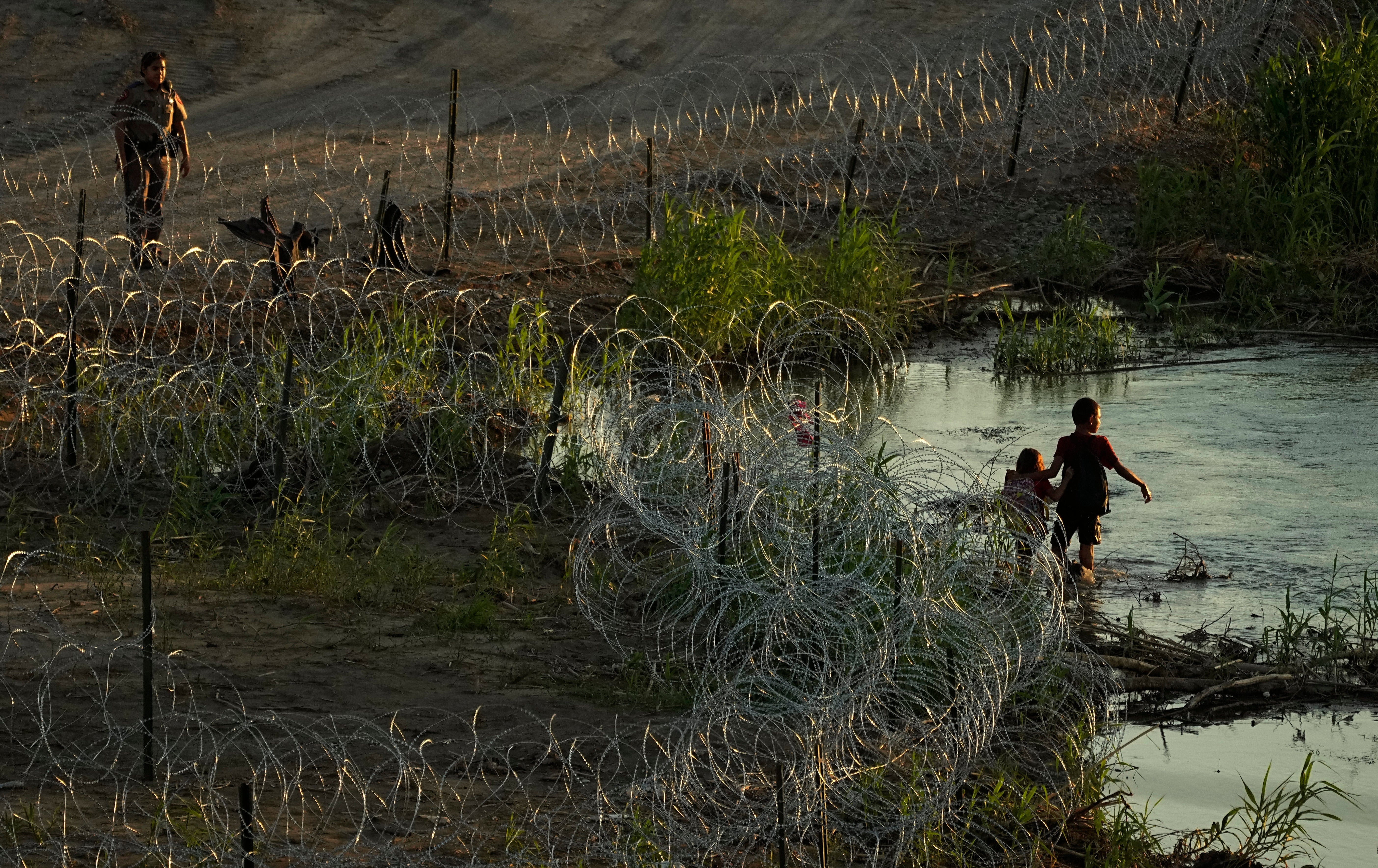 Migrants walk along concertina wire as they try to cross the Rio Grande at the Texas-U.S. border in Eagle Pass, Texas, Thursday, July 6, 2023