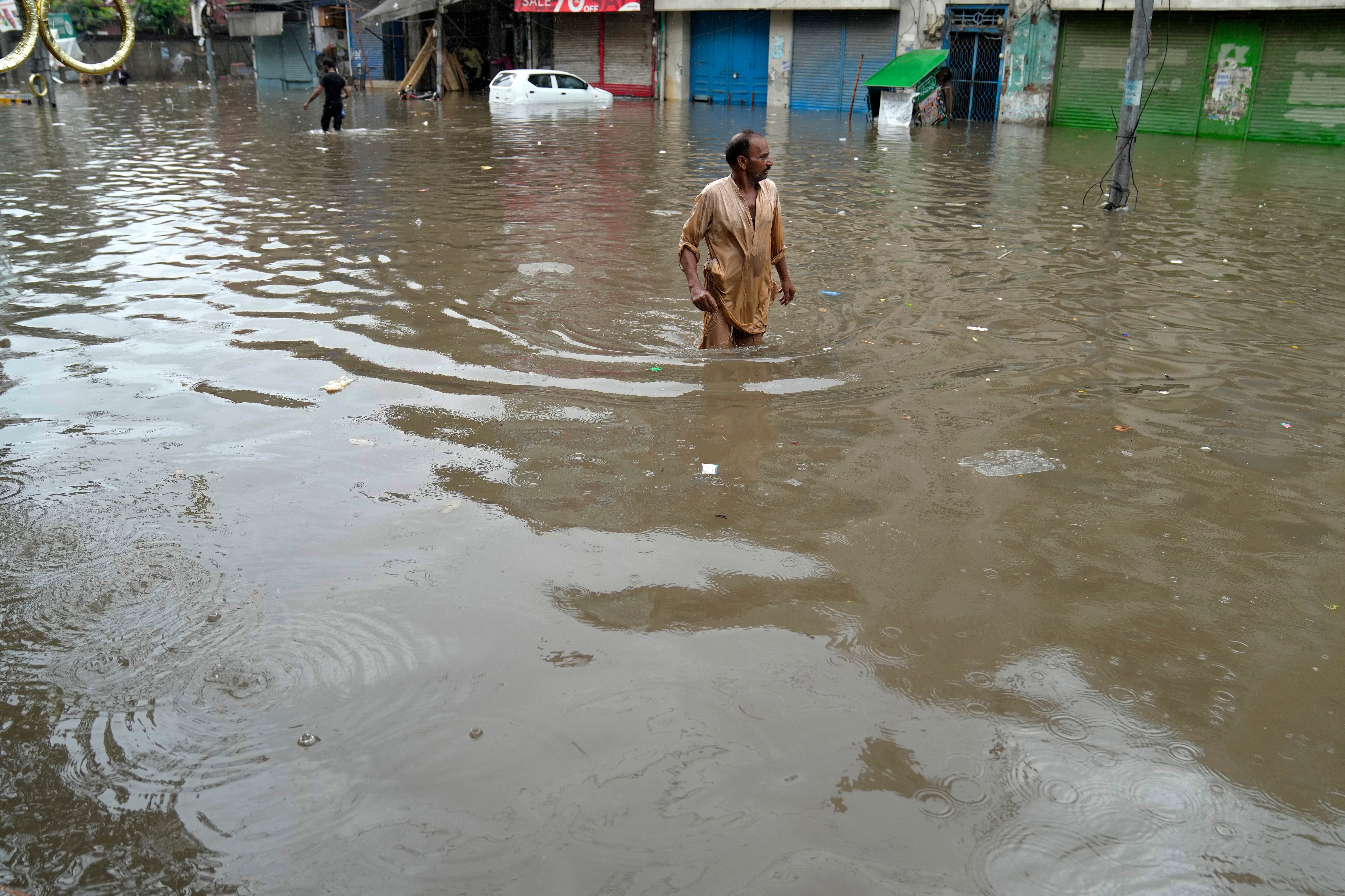 People wade through a flooded area caused by heavy monsoon rainfall in Lahore, Pakistan