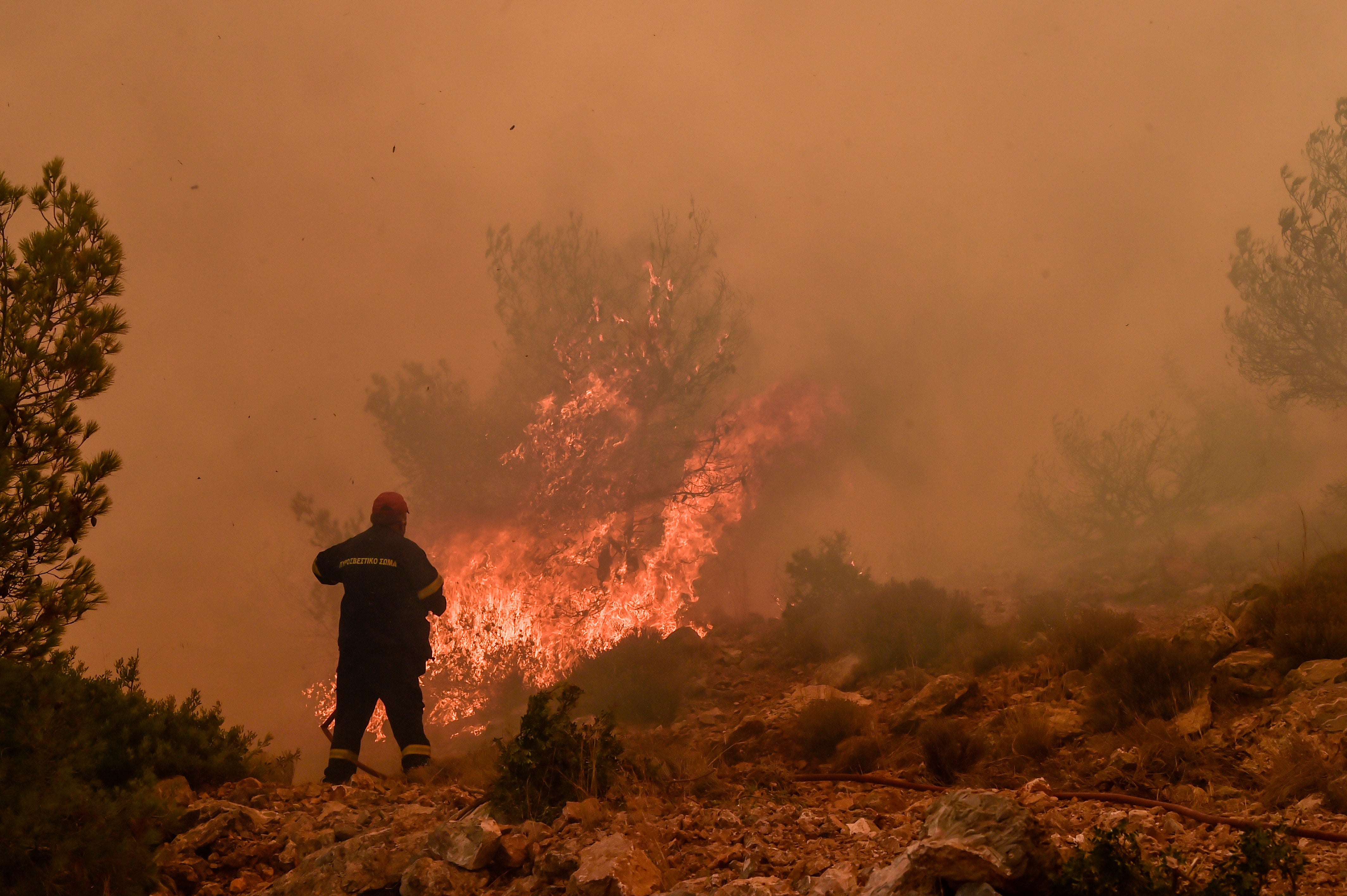 Locals help a firefighter as they try to extinguish a wildfire burning near the village Vlyhada near Athens