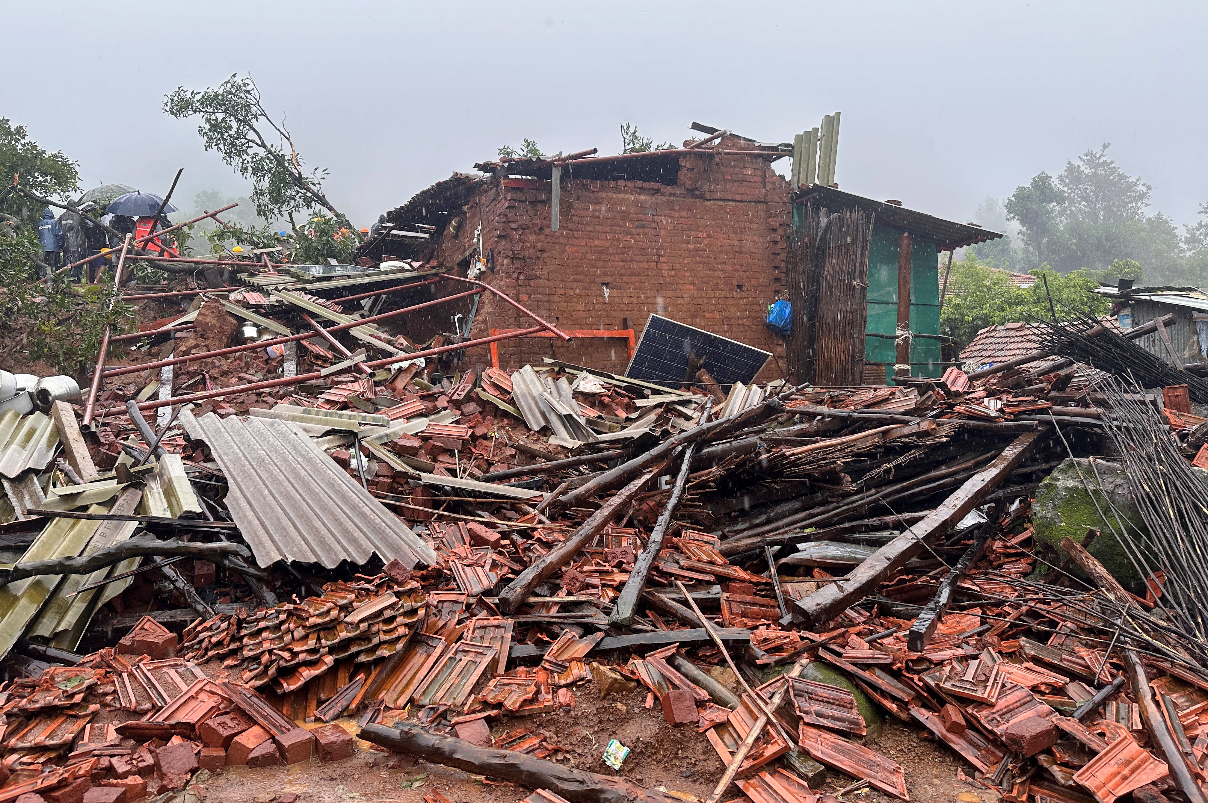 Rescuers stand next to debris of a residential house that was damaged by a landslide in Raigad district