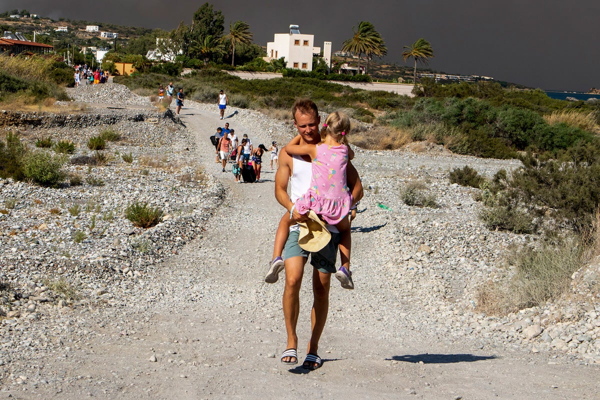 <p>A man carries a child as they leave an area where a forest fire burns on the island of Rhodes</p>