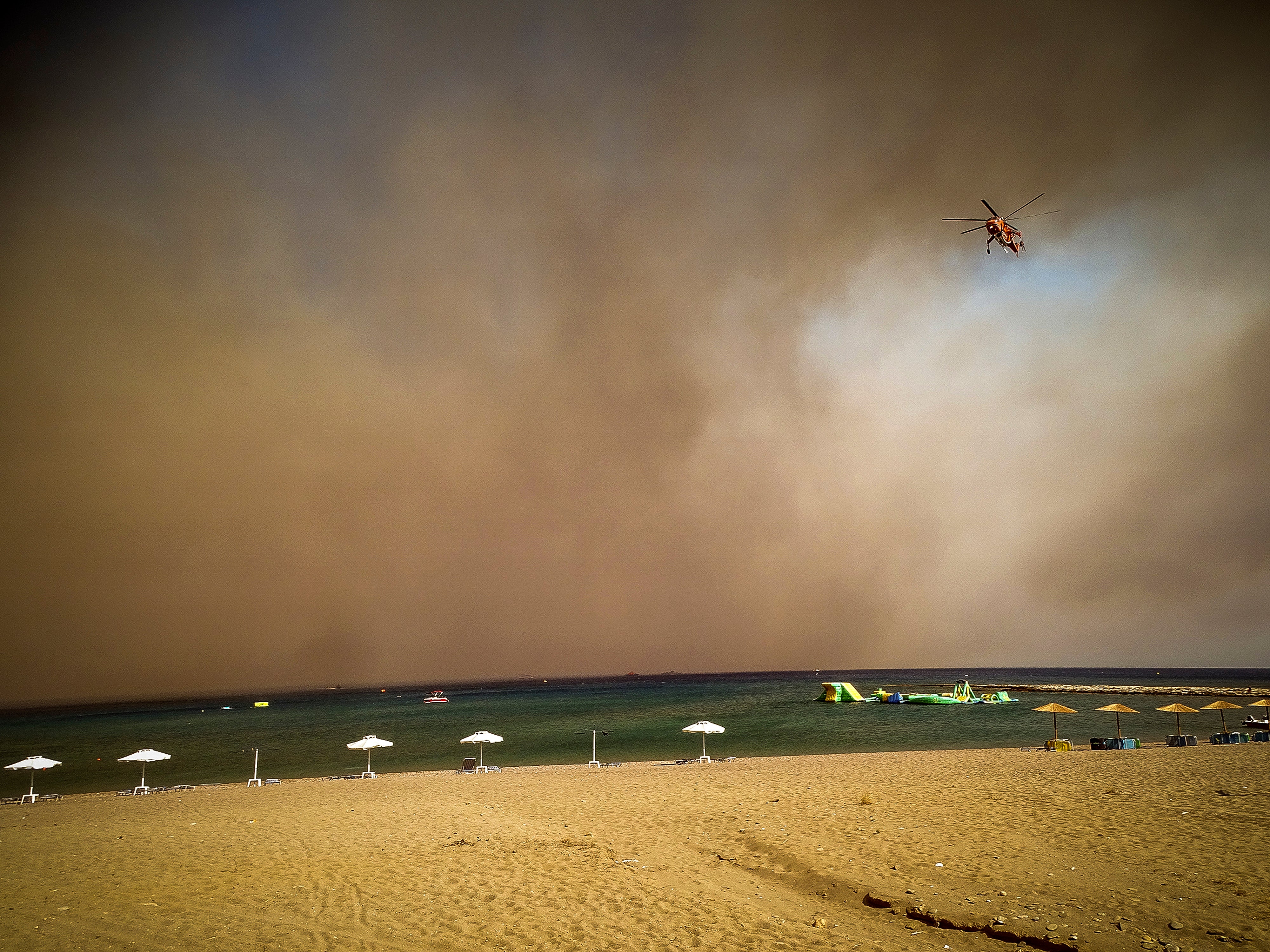 <p>A firefighting helicopter flies over a beach during a forest fire on the island of Rhodes</p>