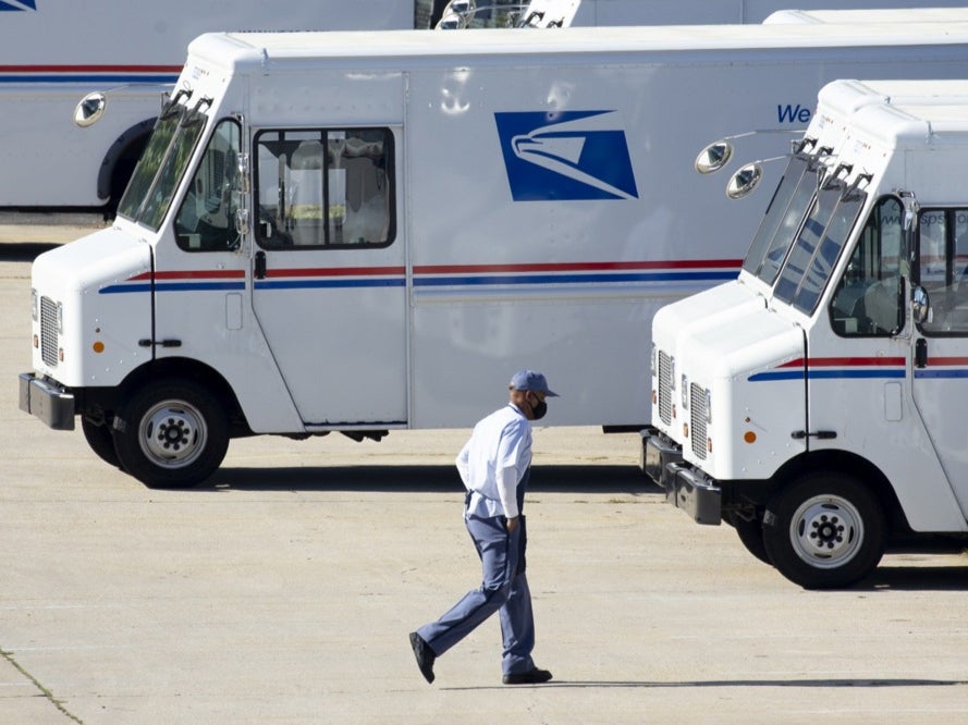 <p>A mail carrier walks to a truck at a United States Postal Service (USPS) processing and distribution center in Washington, DC, on 8 October 2020</p>