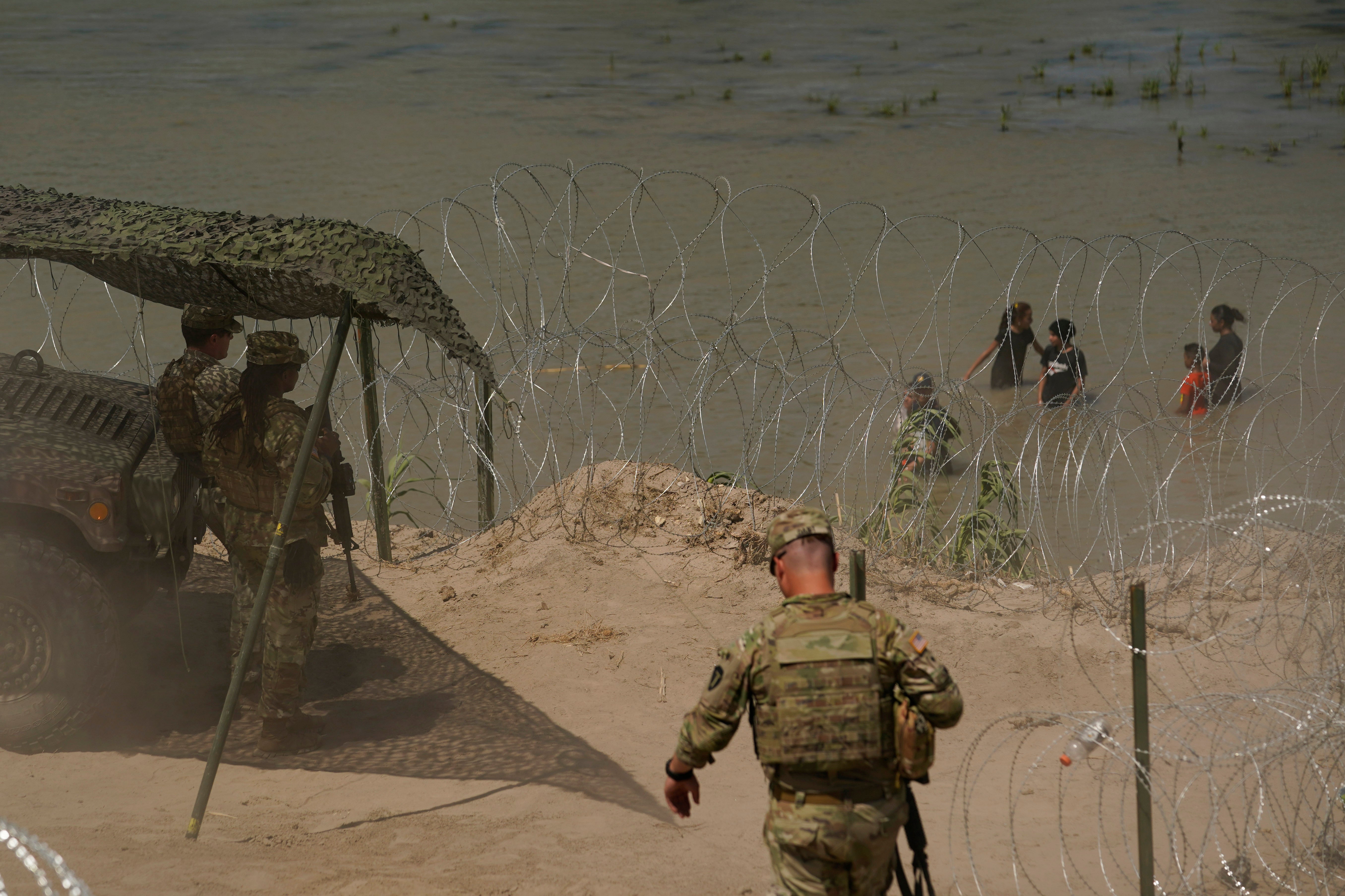 Guardsmen watch as migrants try to cross the Rio Grande from Mexico into the U.S. near in Eagle Pass, Texas, Tuesday, July 11, 2023