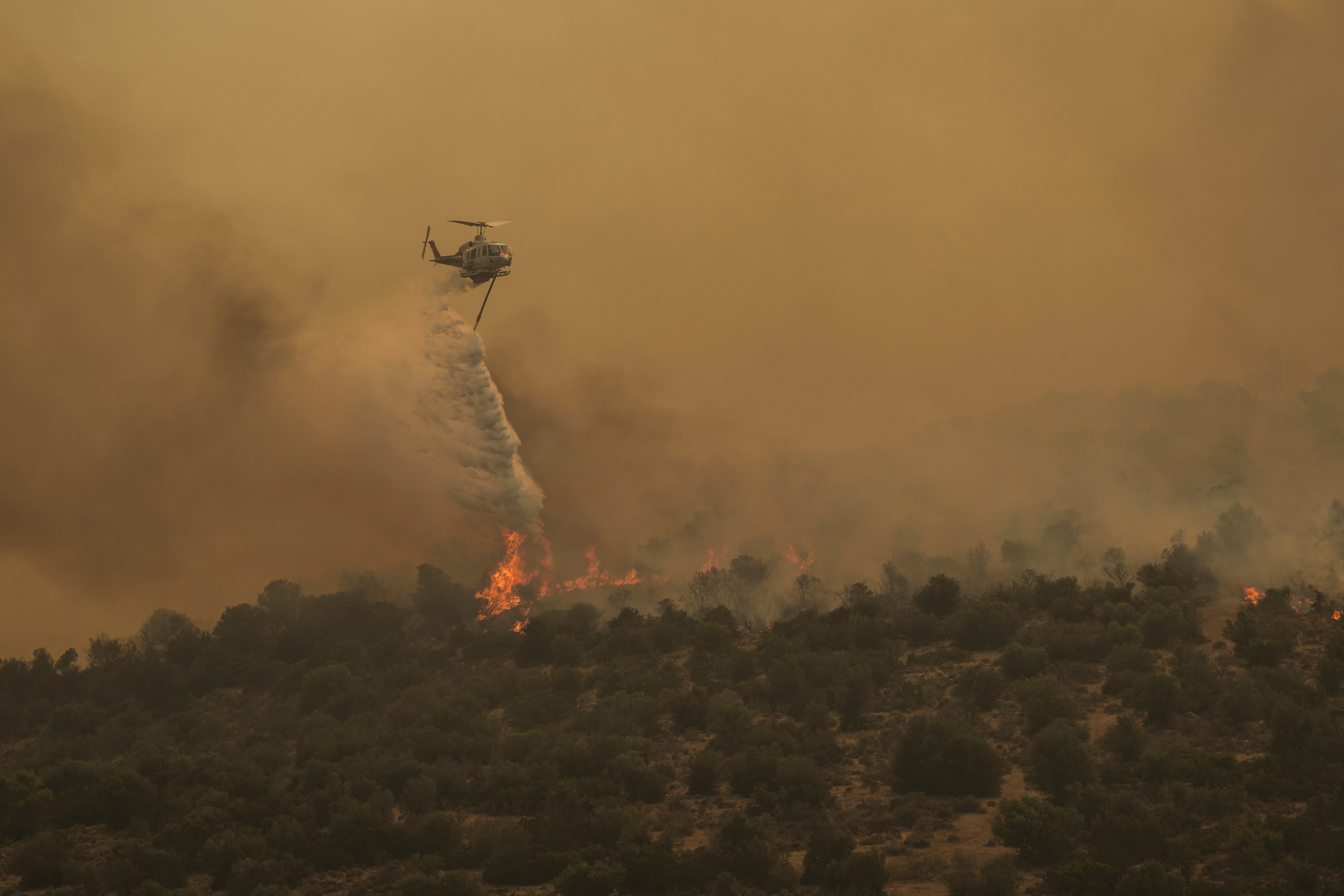 A firefighting helicopter dumps water in Mandra, west of Athens, on 18 July 2023. Another heatwave is expected to hit Greece today