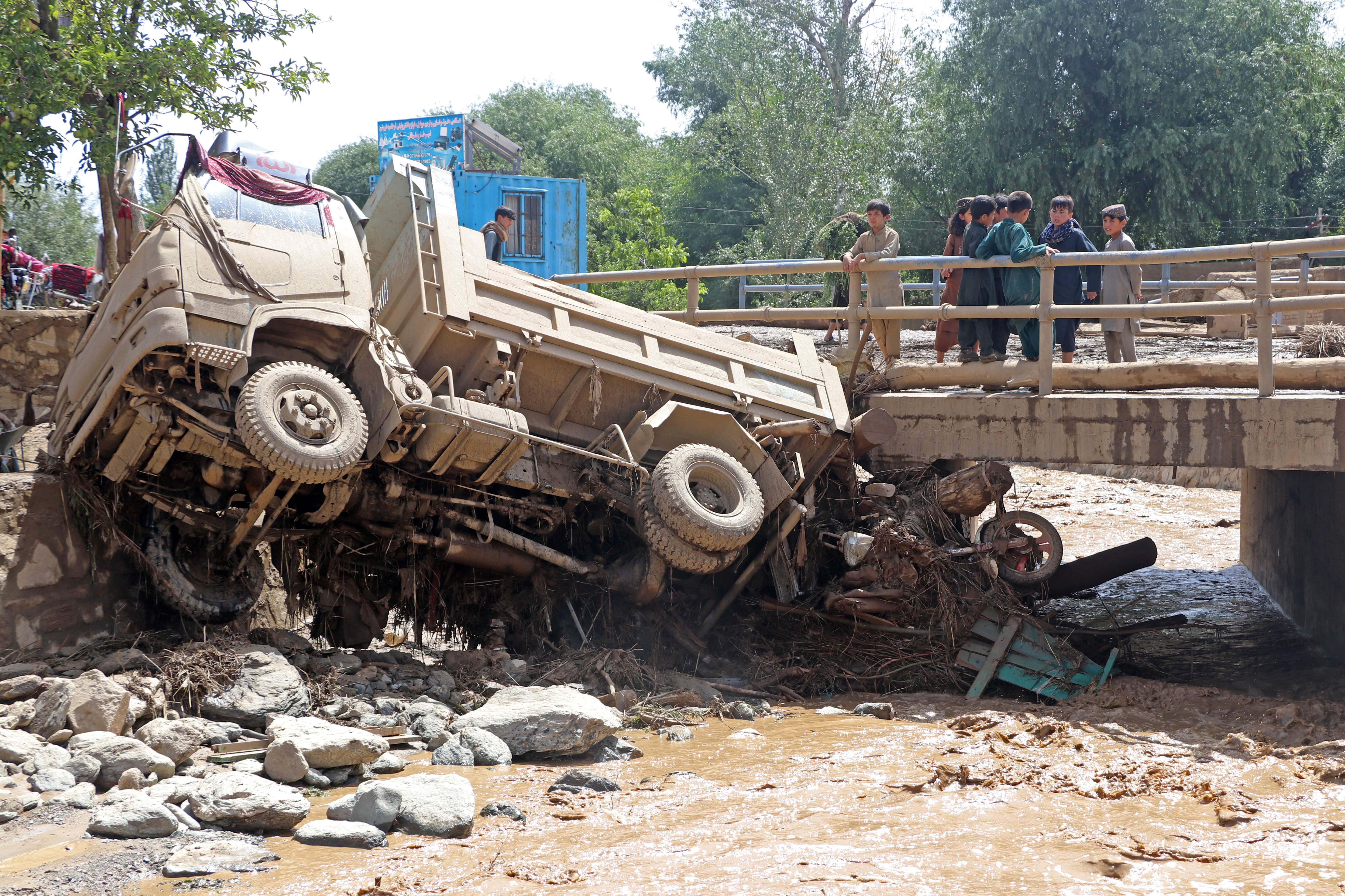 Afghan boys look at a truck that was damaged in flash floods in the Jalrez district of Maidan Wardak province