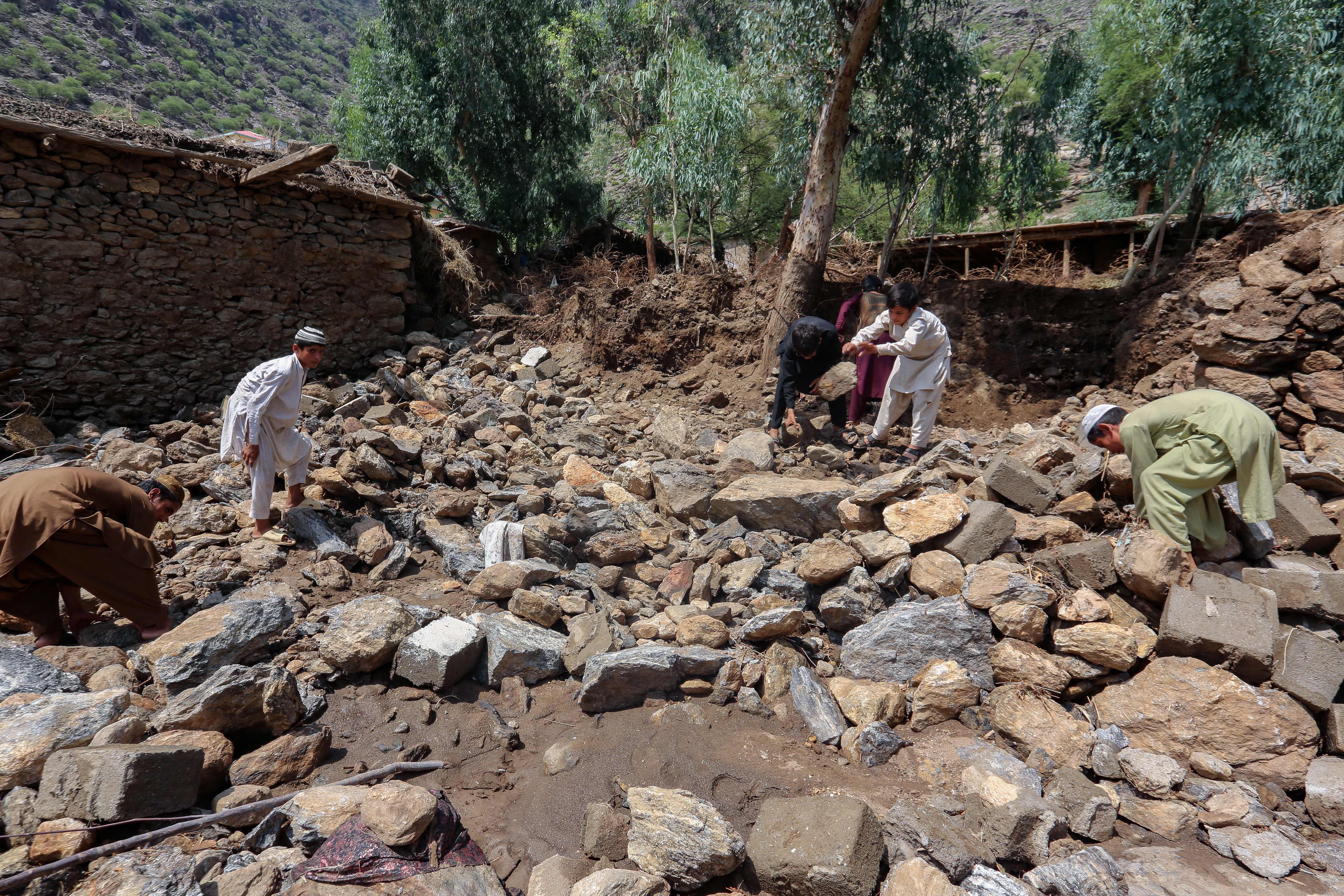 Afghan villagers clean debris next to their houses damaged in flash floods in Watapur district of Kunar province