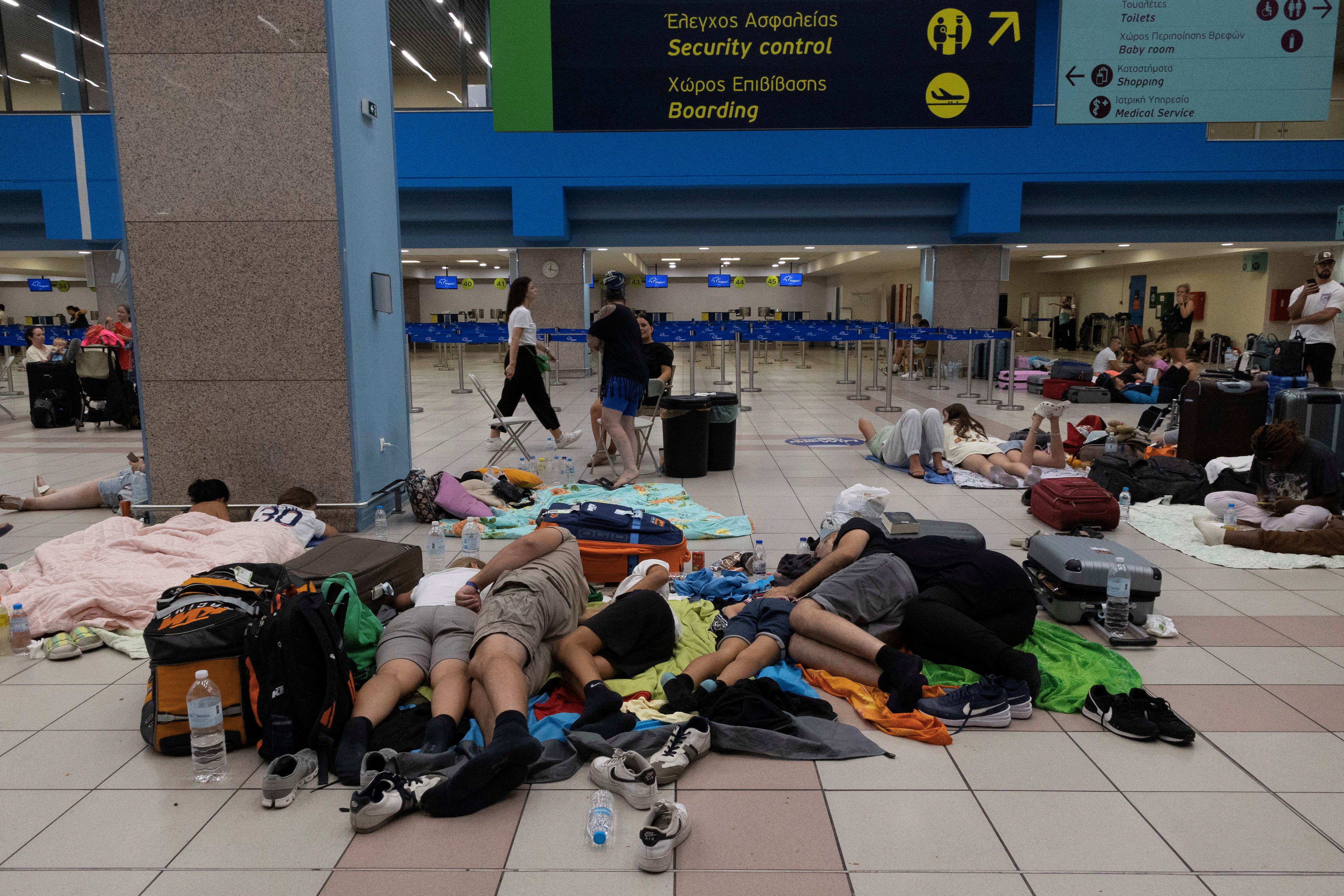 Tourists sleep as they wait for departing planes at the airport, after being evacuated following a wildfire on Rhodes