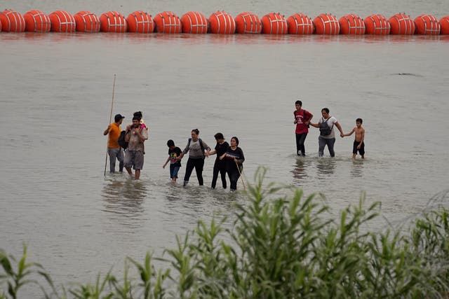 <p>Migrants who crossed the Rio Grande from Mexico walk past large buoys being deployed as a border barrier on the river in Eagle Pass, Texas, Wednesday, July 12, 2023. The floating barrier is being deployed in an effort to block migrants from entering Texas from Mexico</p>