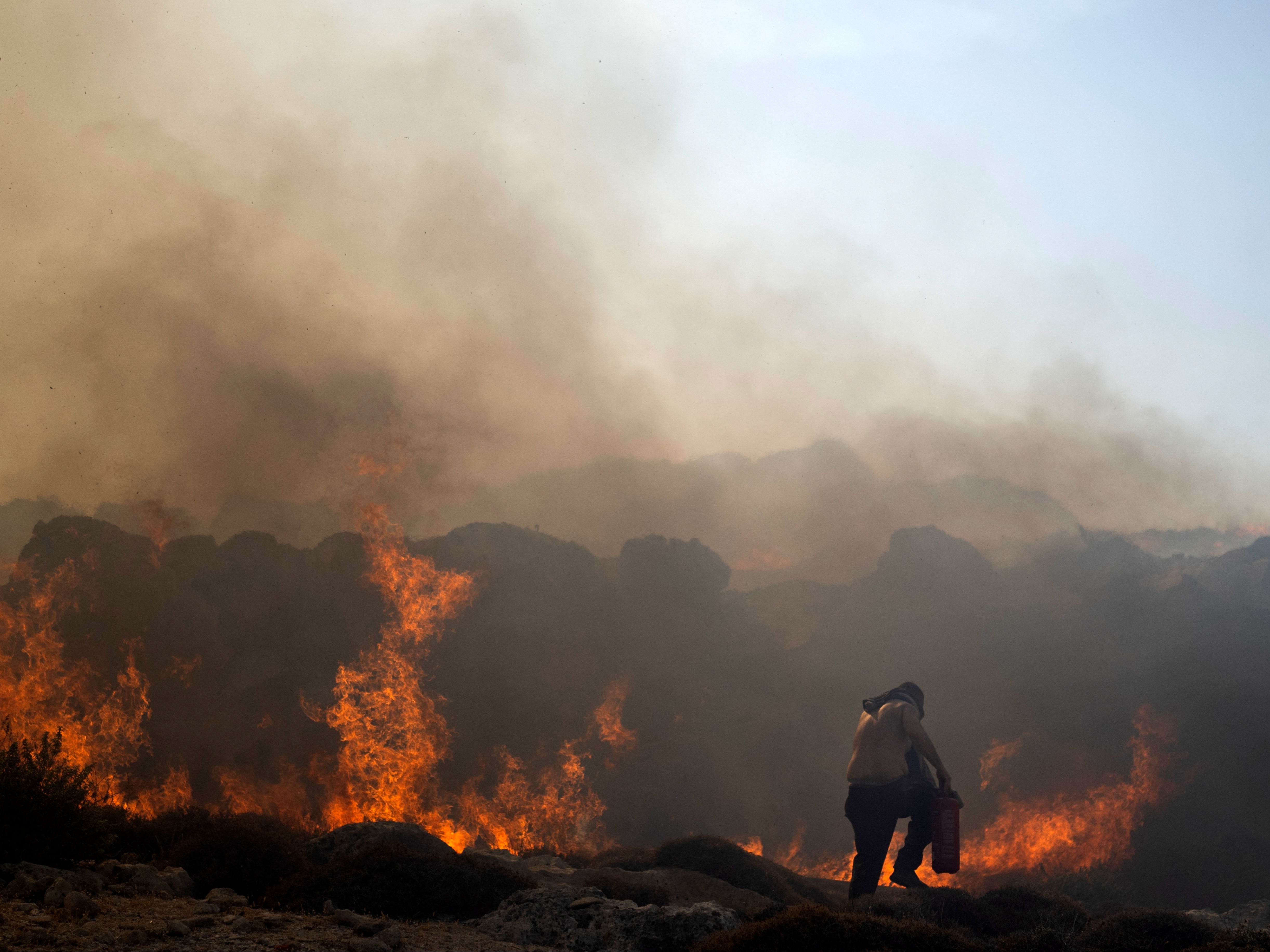 A man tries to extinguish a fire, near the seaside resort of Lindos, on the Aegean Sea island of Rhodes, southeastern Greece