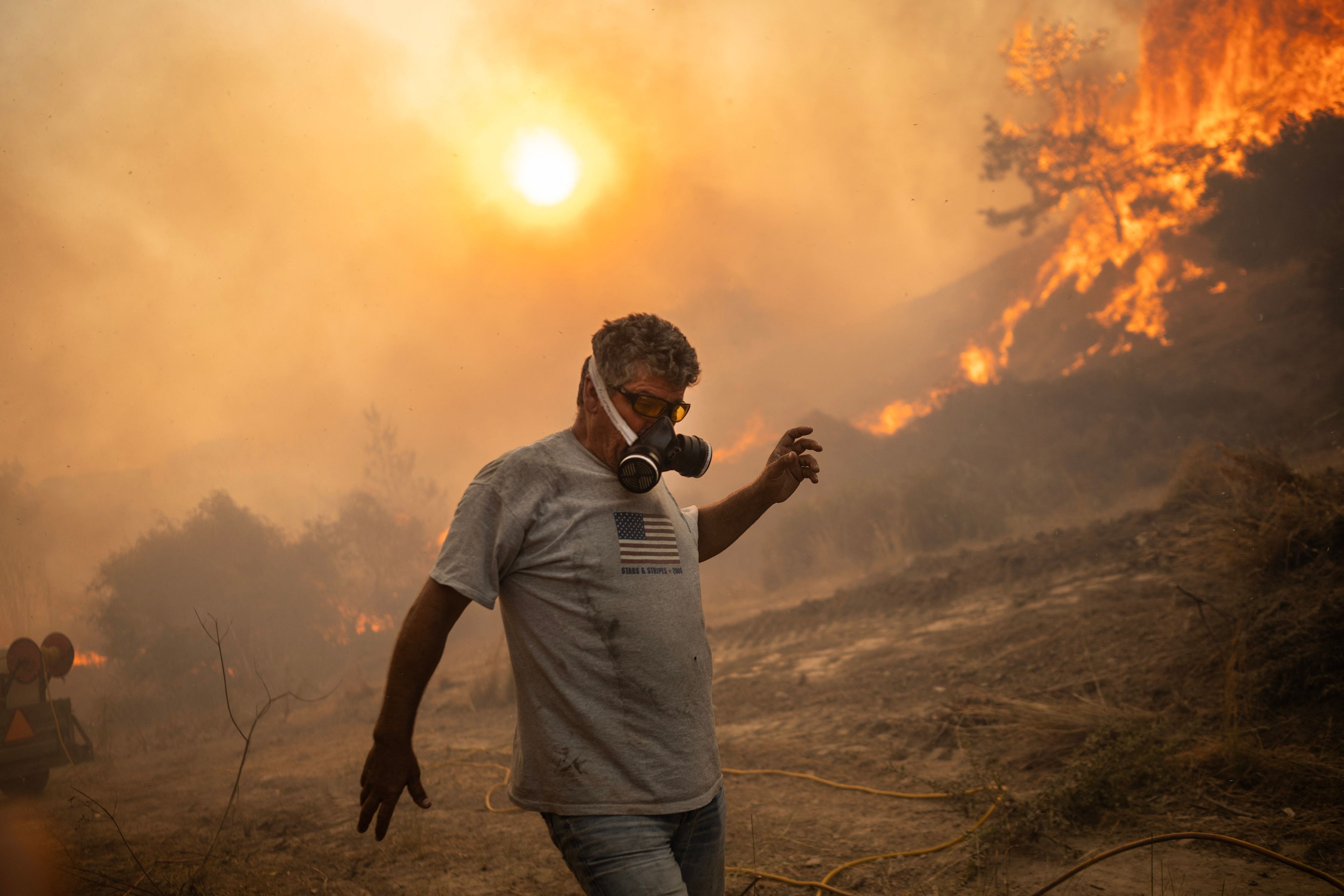 <p>A wearing breathing protection man reacts as a fire burns into the village of Gennadi on the Greek Aegean island of Rhodes</p>