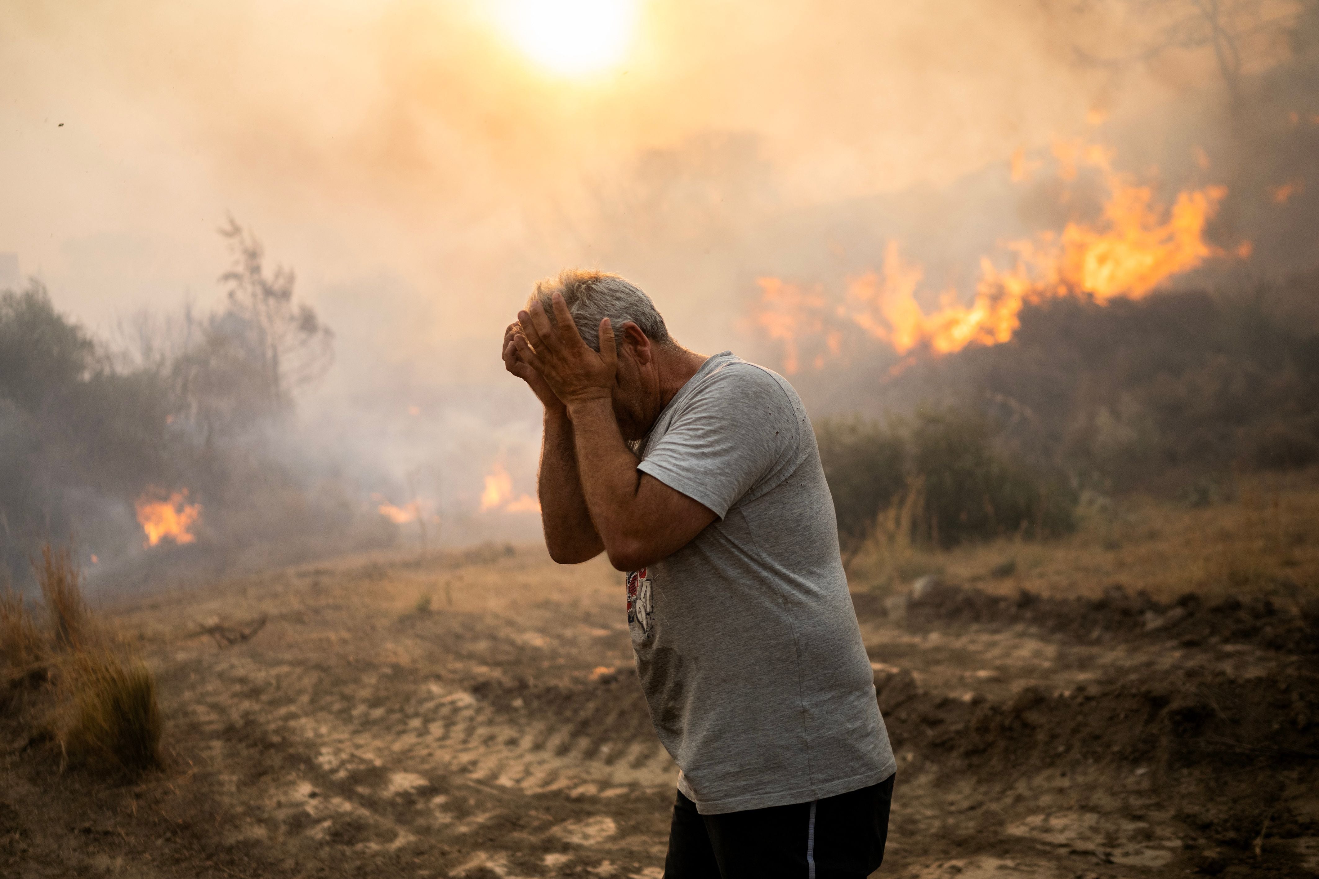 <p>A man reacts as a fire burns in a village on the Greek Aegean island of Rhodes</p>