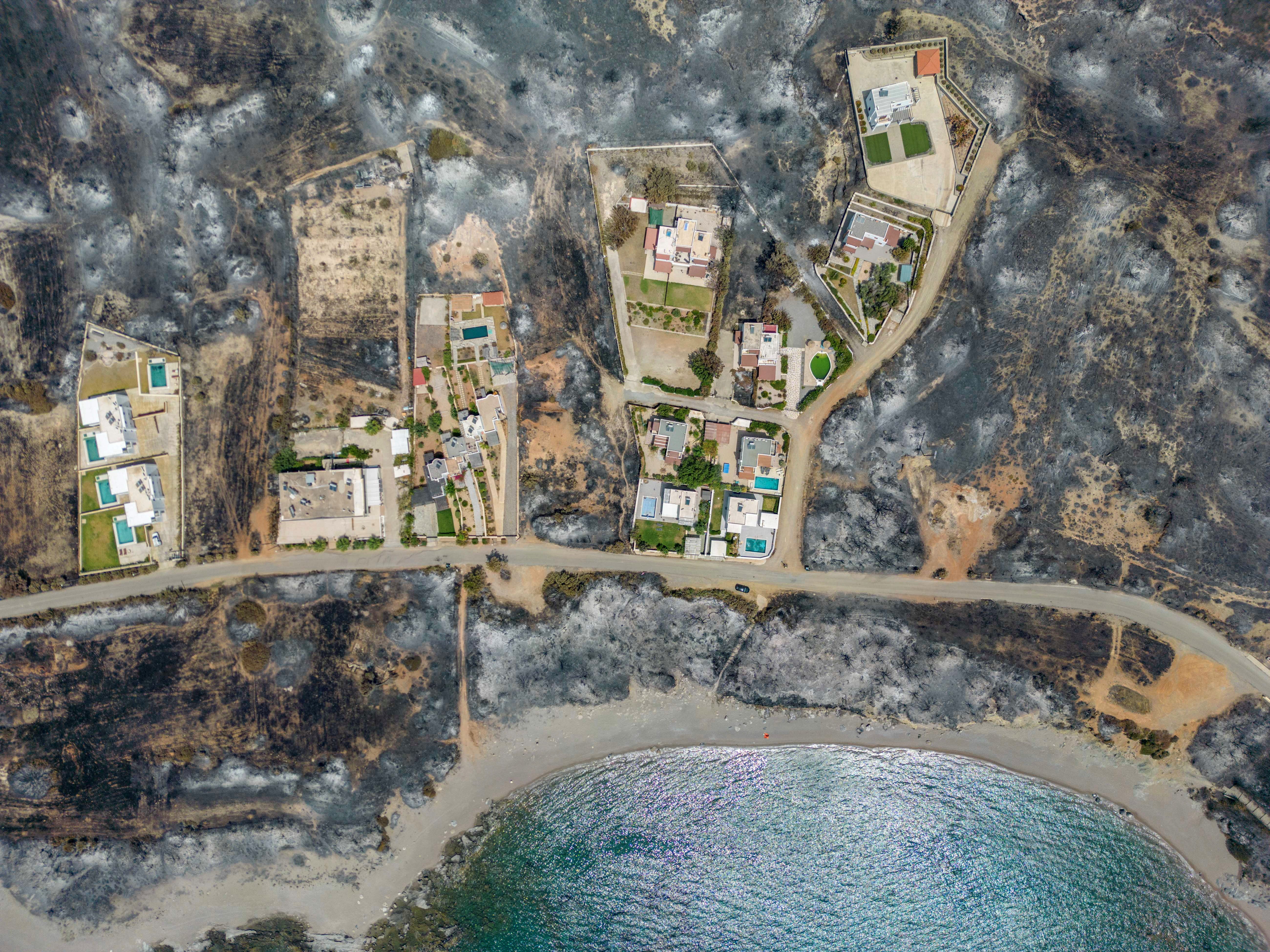 An aerial view of houses among burned land, as a wildfire burns on the island of Rhodes