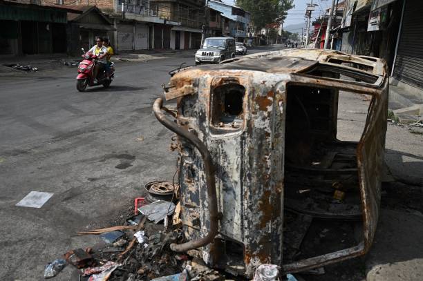 A motorist rides past a burnt vehicle on a street in Churachandpur in violence hit areas of northeastern Indian state of Manipur