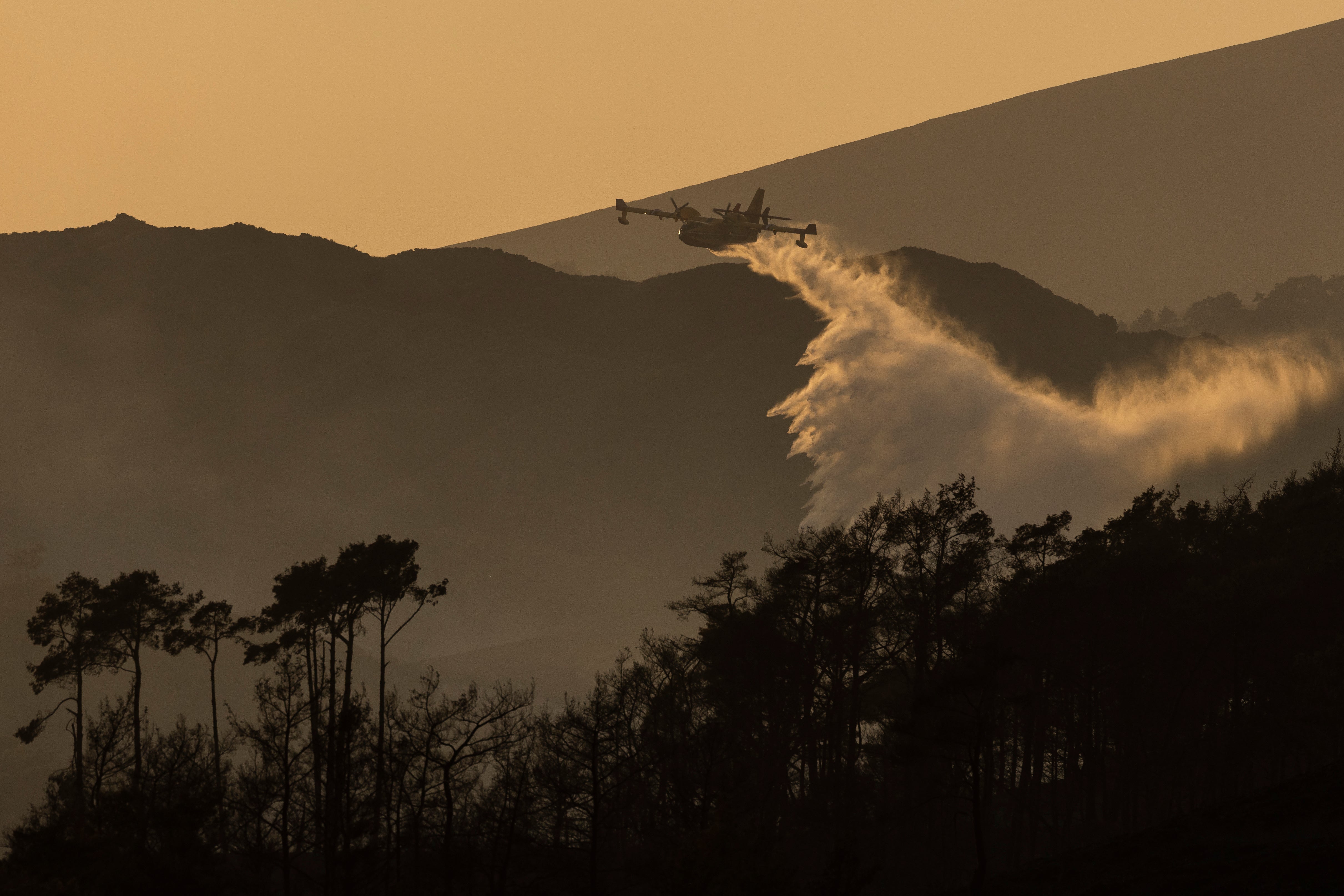 A plane drops water onto flames on a hillside at sunset on July 27, 2023 in Vati, Rhodes