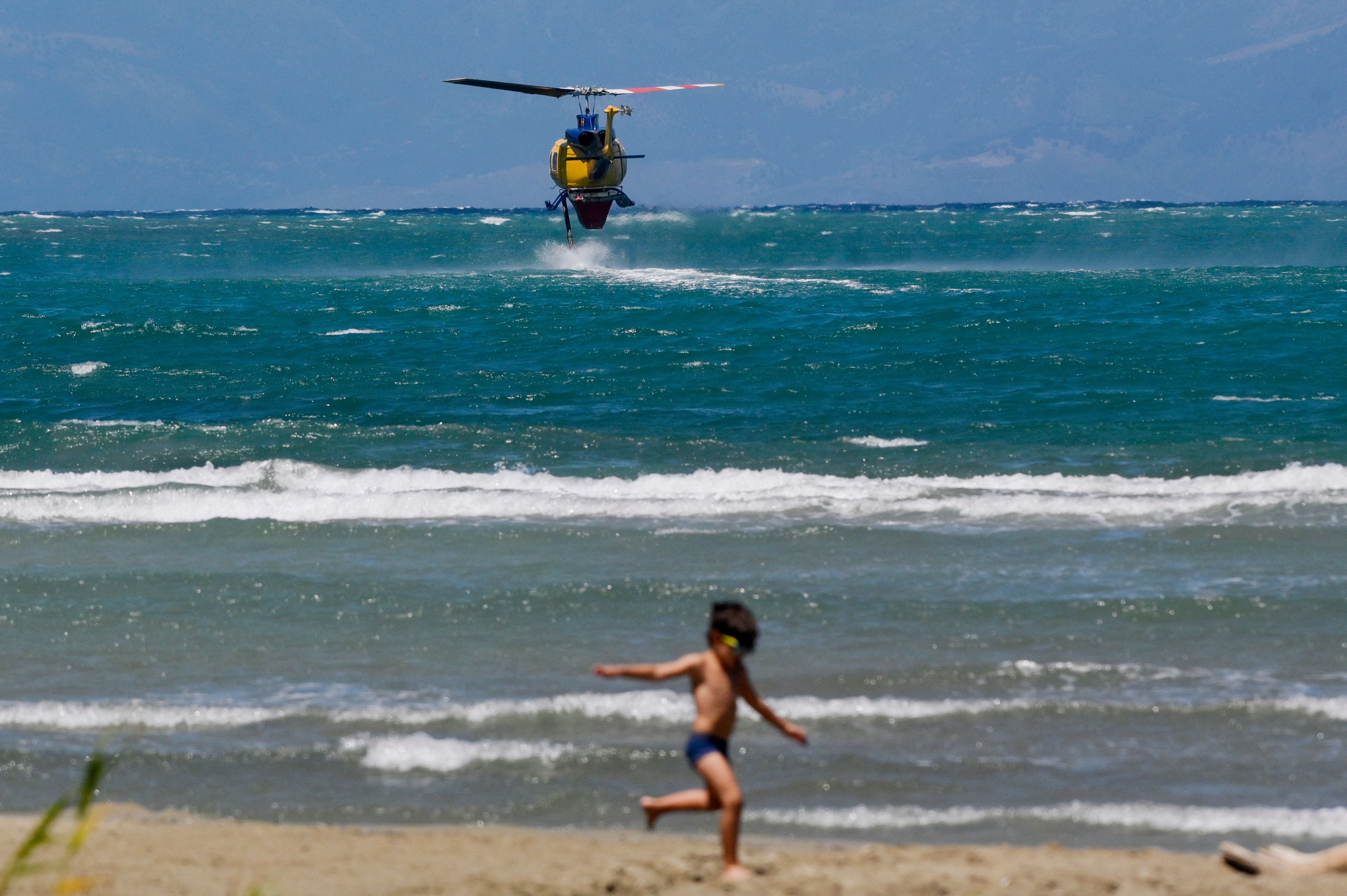 A boy plays on the beachfront as a firefighting helicopter hovers above the sea to refill water for a drop on wildfires near the village of Loutses on the Greek island of Corfu