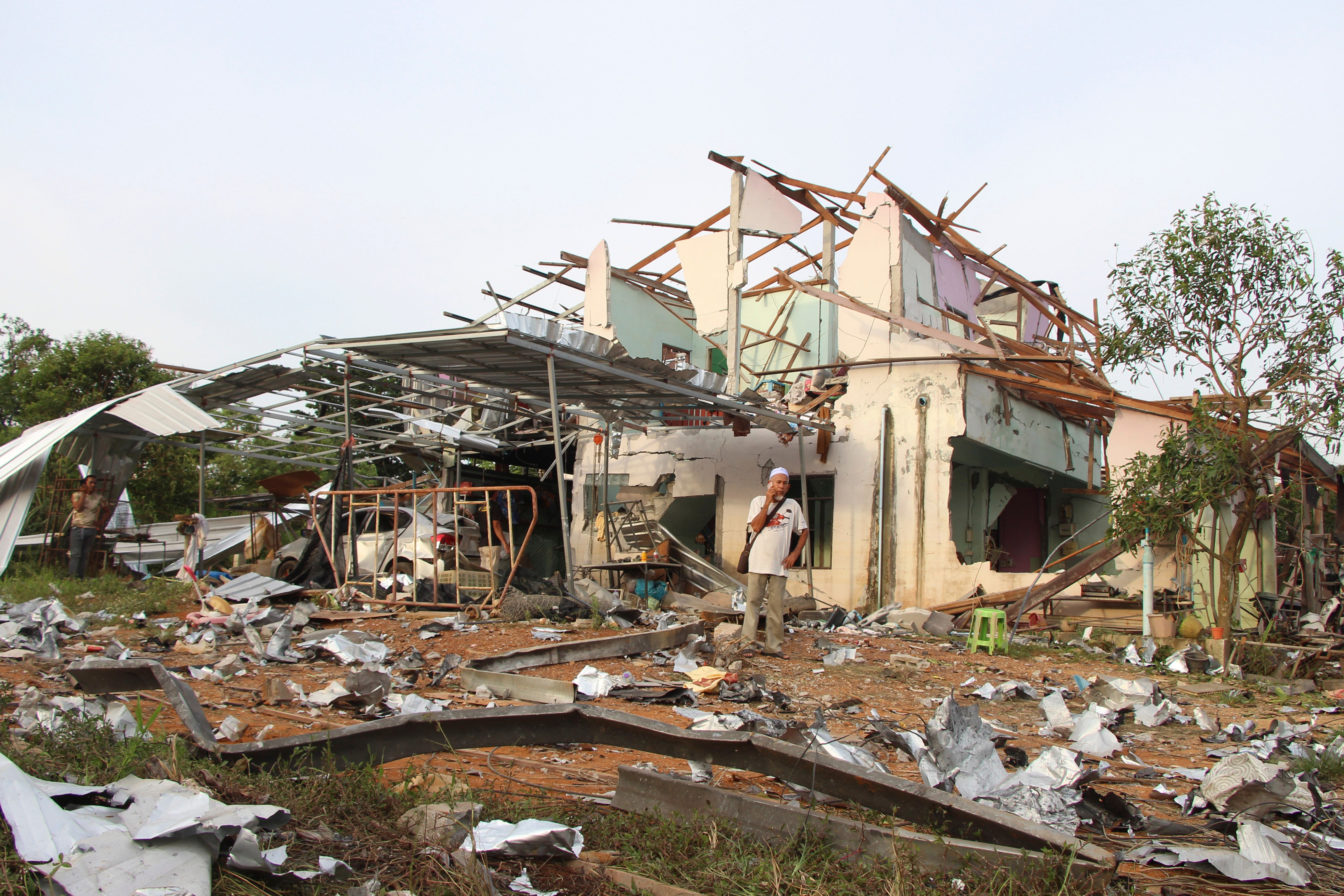 People speak on their phones in front of a house damaged by an explosion at a firework warehouse in Narathiwat province southern Thailand