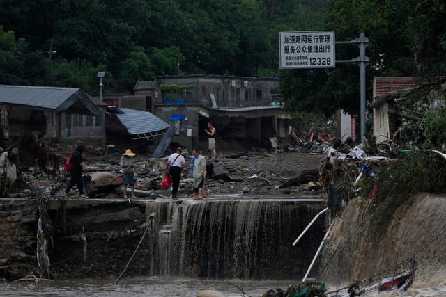 <p>People walk through a village damaged by floodwaters in the Mentougou District as continuous rainfall triggers alerts in Beijing </p>