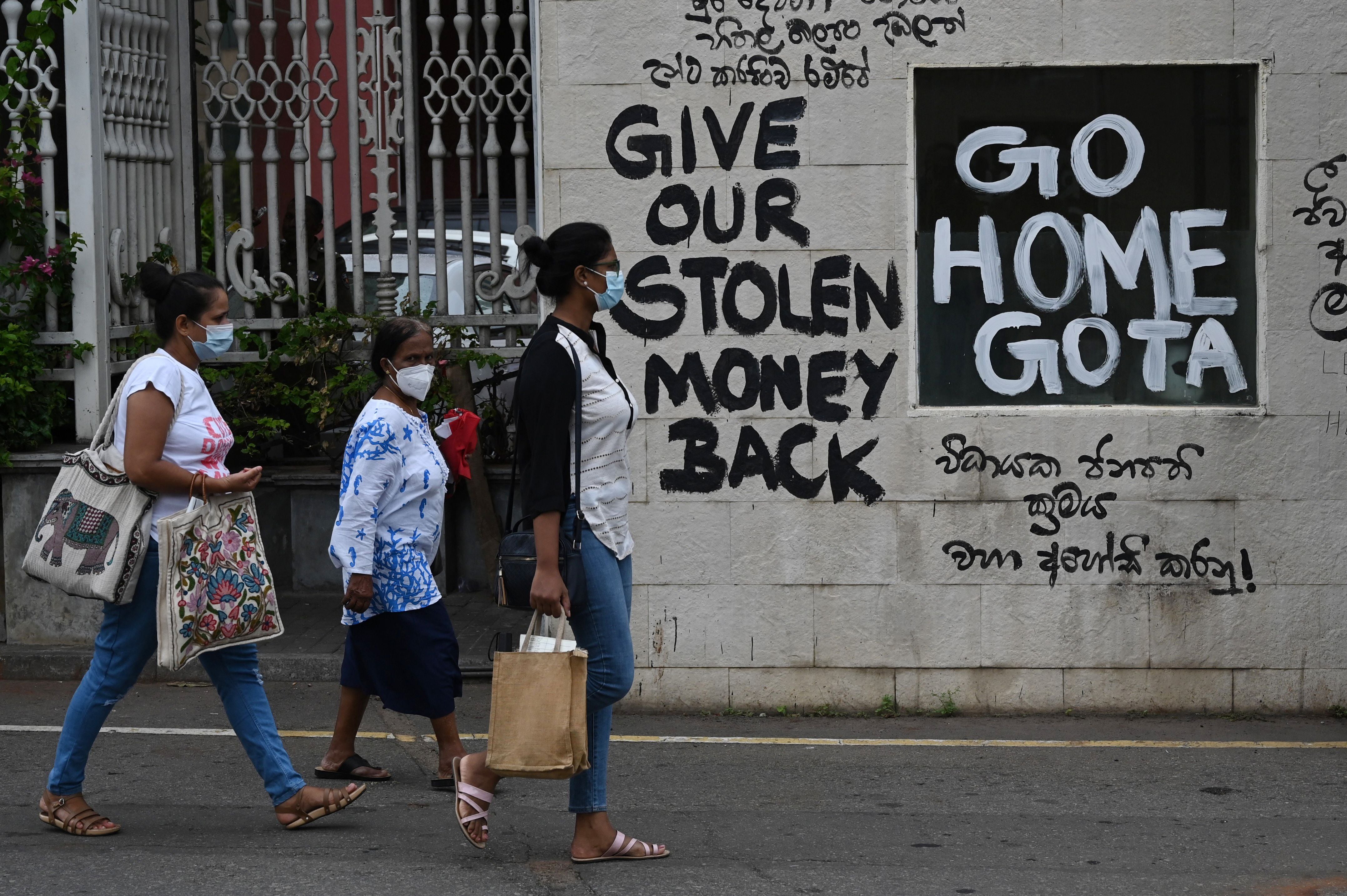 A man rides a bicycle walk past slogans painted on a wall against the government near the presidents office residence in Colombo on 21 July 2022