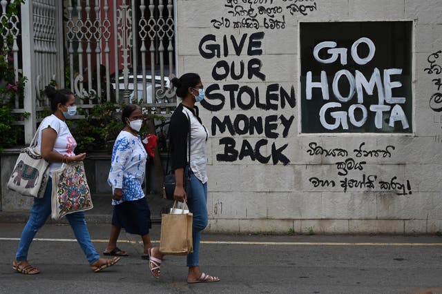 <p>A man rides a bicycle walk past slogans painted on a wall against the government near the presidents office residence in Colombo on 21 July 2022</p>