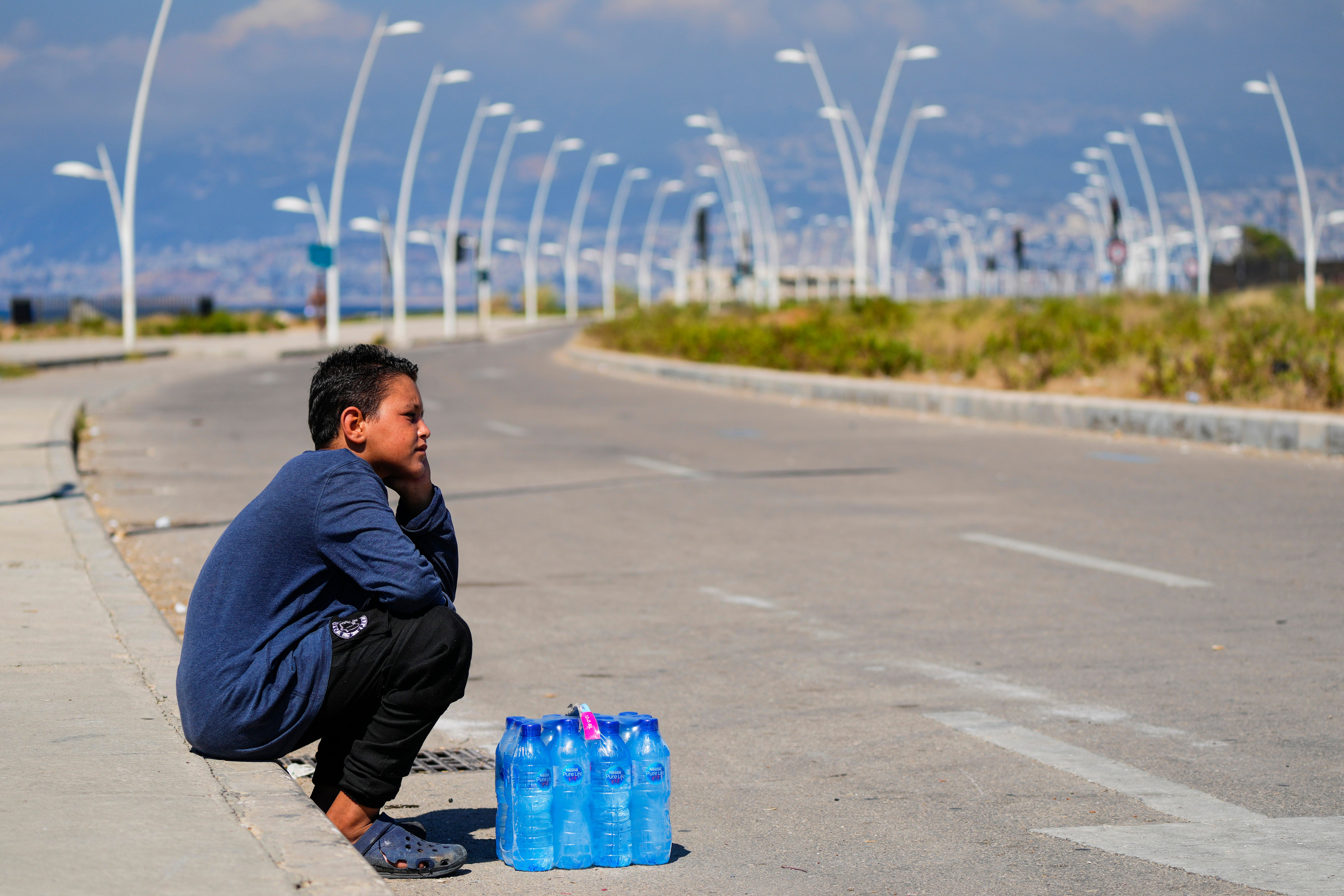 A young boy sits next to a pack of water bottles as he waits for customers during a sweltering day on the Mediterranean Sea corniche in Beirut, Lebanon on July 20, 2023