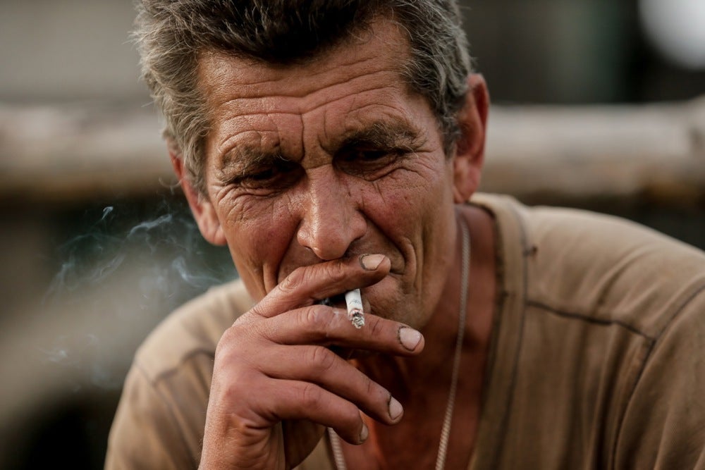 Mykola smokes a cigarette near his house