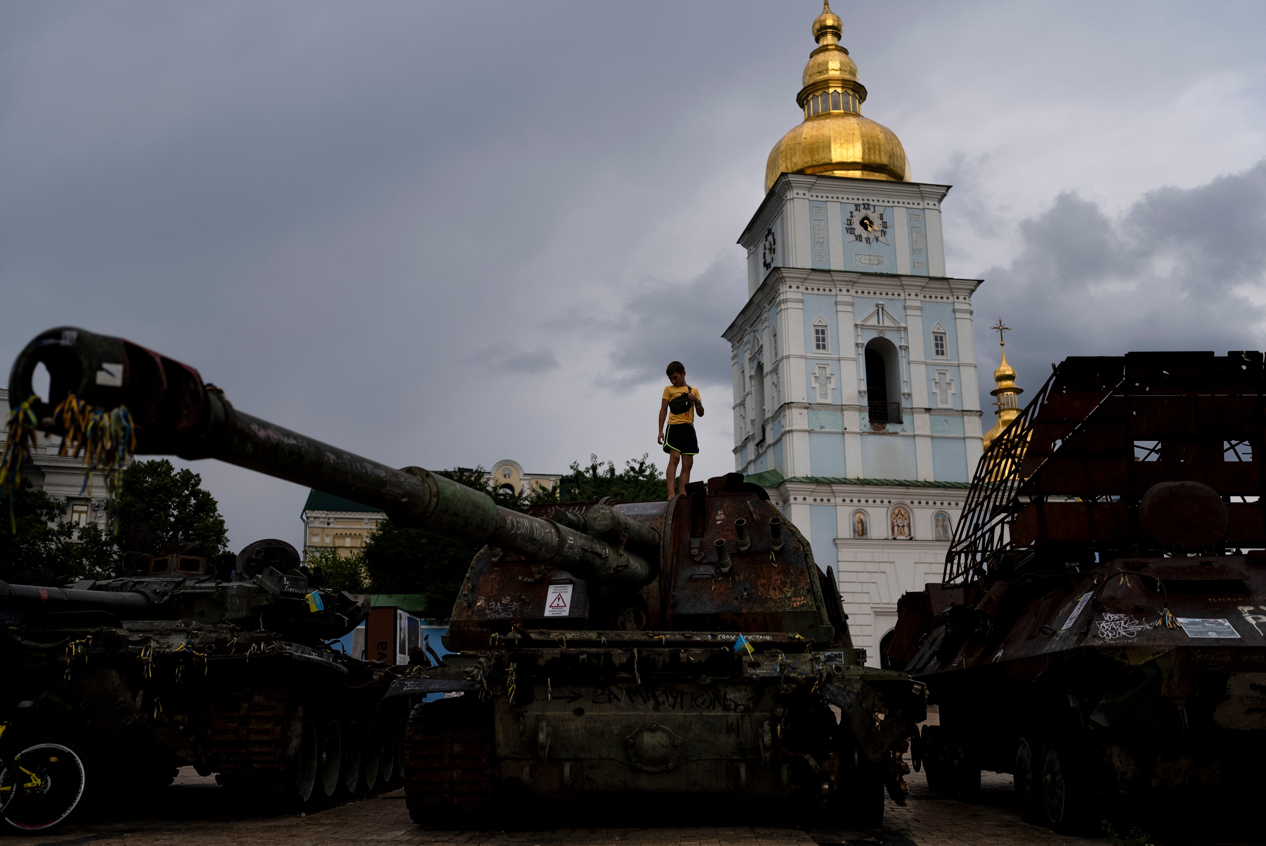 A boy stands on top of a destroyed Russian tank exhibited outside St Michael's Golden-Domed Monastery in Kyiv