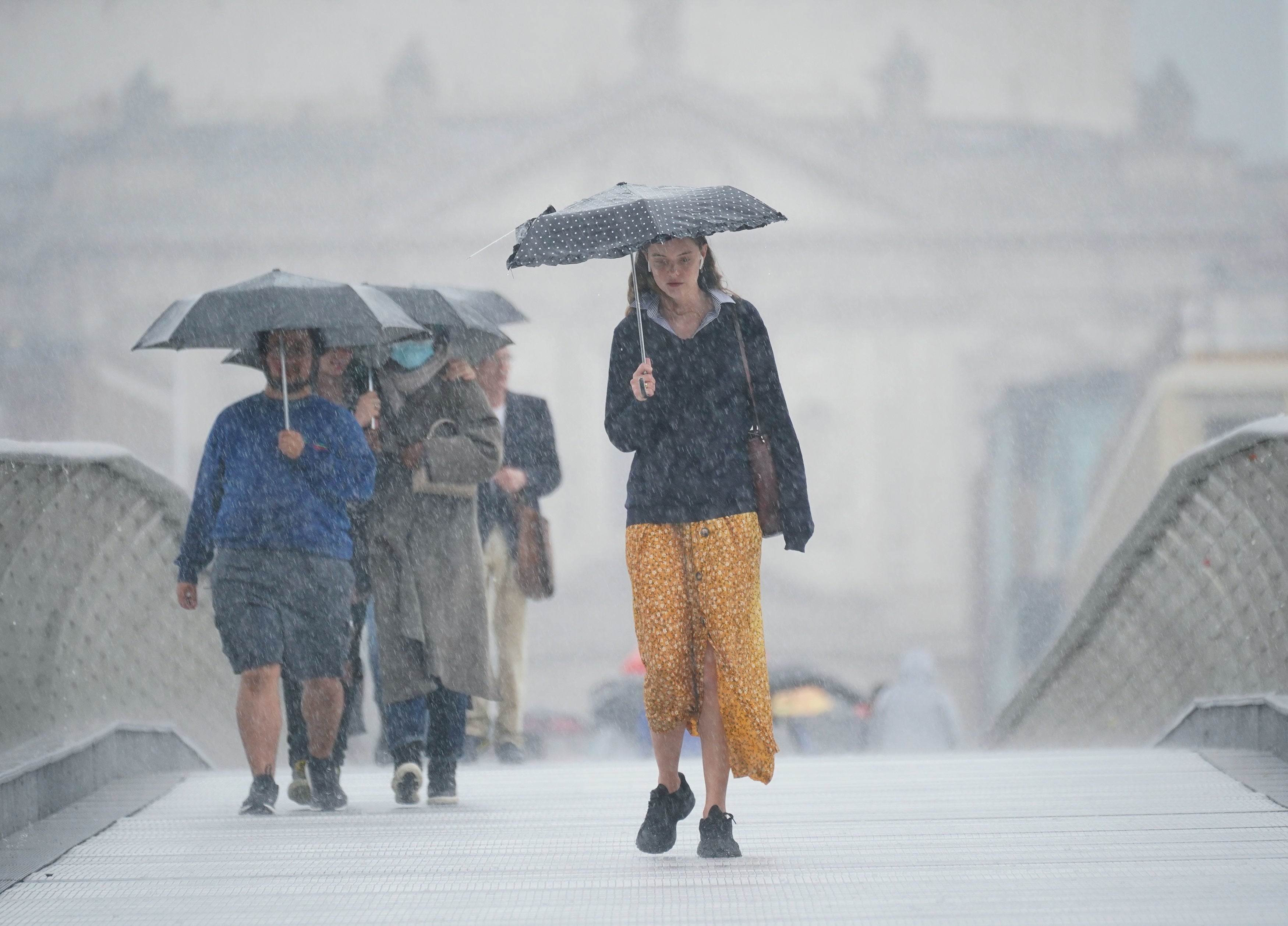 People walking along the Millennium Bridge, London, during a rain shower