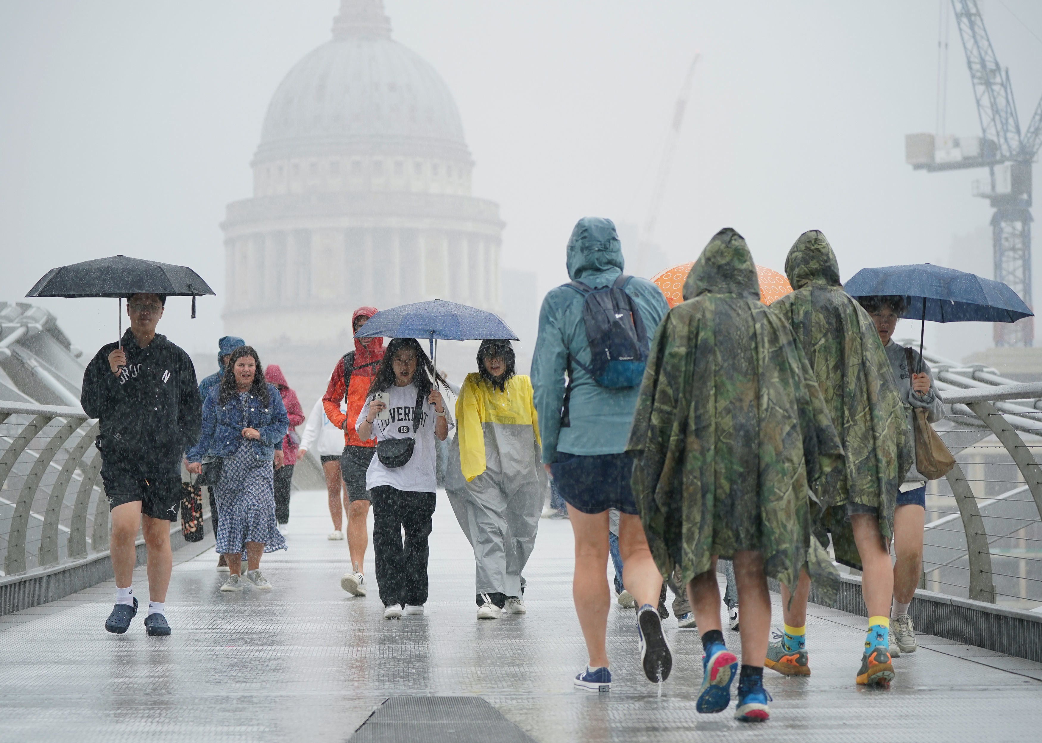 People walking along the Millennium Bridge in London during a rain shower, Wednesday 2 August