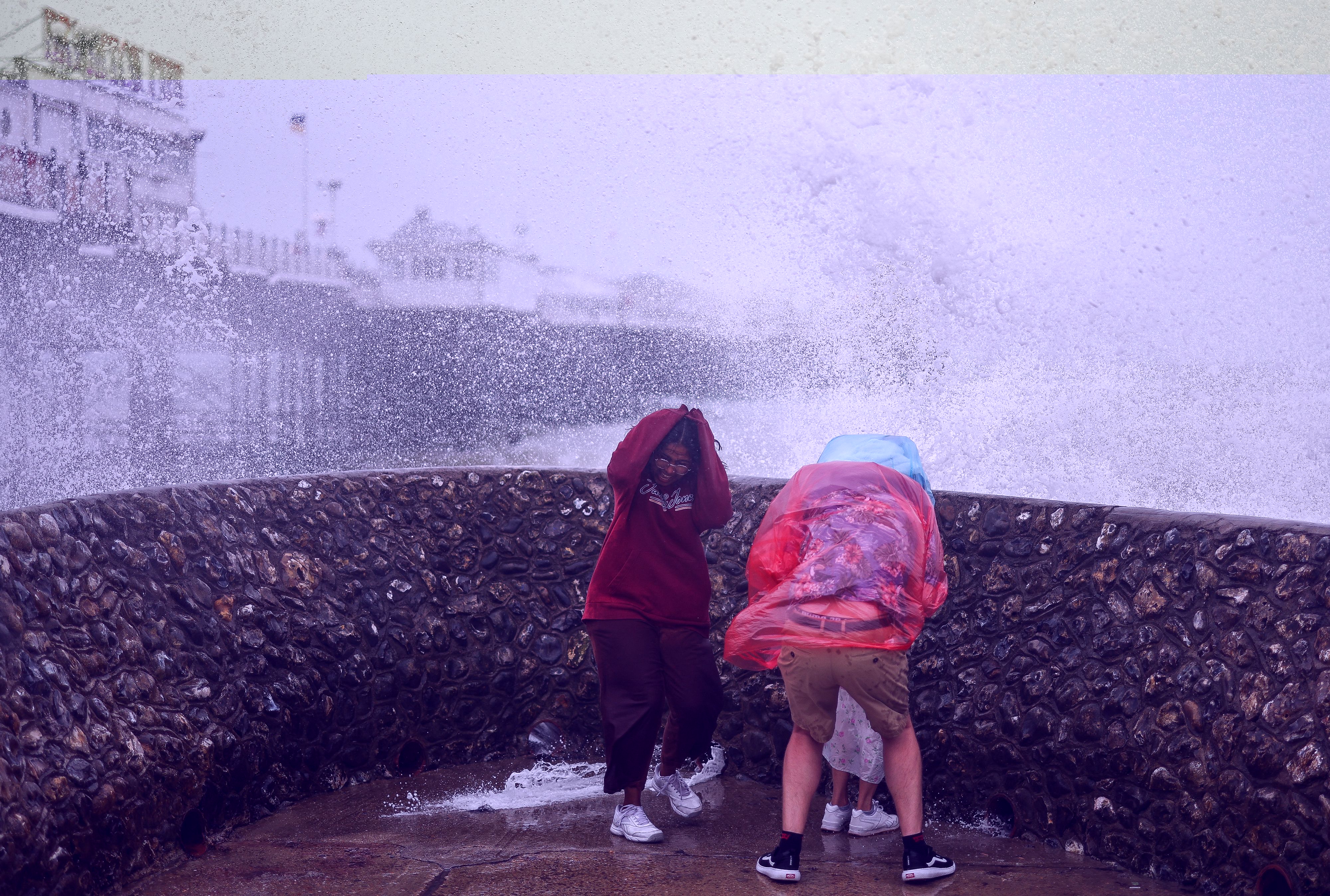 People react as a wave hits a seawall next to the Palace Pier in Brighton, southern England on August 5, 2023, as Storm Antoni brings rain and high winds to the UK.