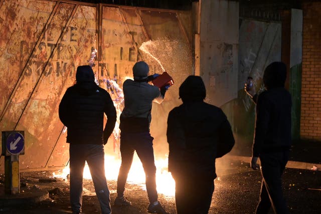<p>Petrol is poured as youths exchange projectiles through the Peace Gate with their faces covered during clashes in April 2021</p>