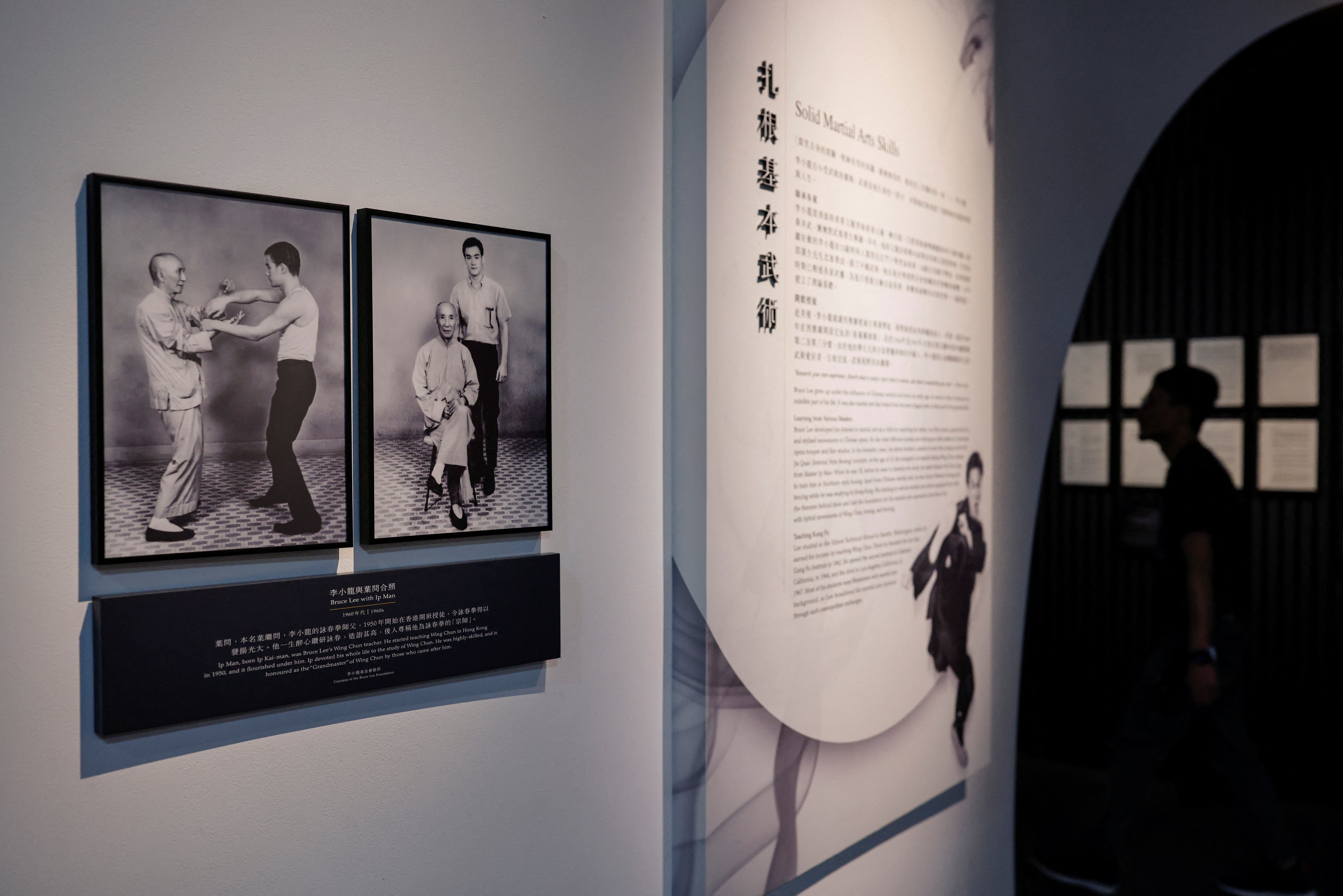 A man walks near photos of Wing Chun grandmaster Ip Man and his student Bruce Lee, at the Hong Kong Heritage Museum